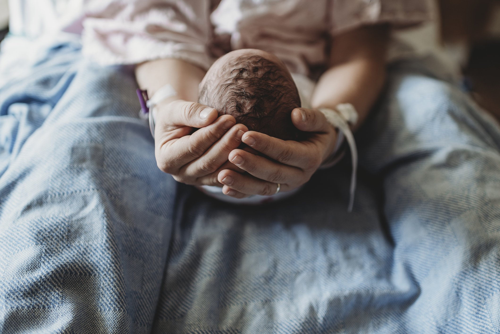Makroansicht der Hände der Mutter, die den Kopf des neugeborenen Jungen halten | Getty Images