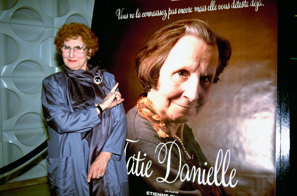 Tsilla Chelton se tient près de l'affiche de son film de 1990, Tatie Danielle, alors qu'elle assiste à la première du film à Biarritz, en France. | Photo : Getty Images