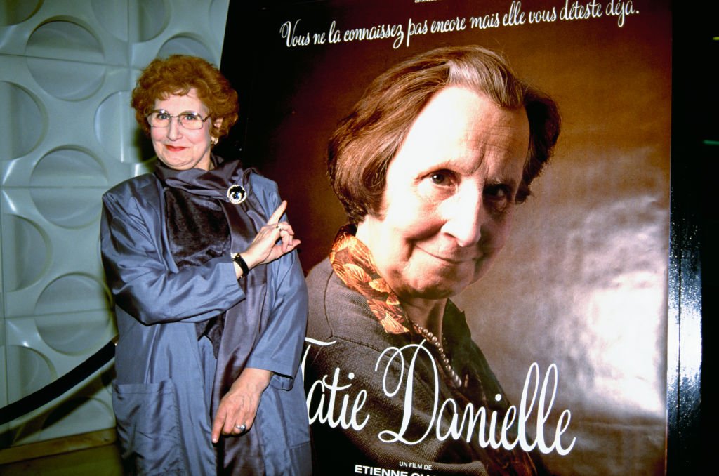 Tsilla Chelton se tient près de l'affiche de son film de 1990, Tatie Danielle, alors qu'elle assiste à la première du film à Biarritz, en France. | Photo : Getty Images Tsilla Chelton se tient près de l'affiche de son film de 1990, Tatie Danielle, alors qu'elle assiste à la première du film à Biarritz, en France. | Photo : Getty Images