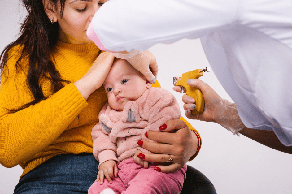 Mutter hält Baby, während Arzt sich bereit macht, die Ohren des Kindes zu piercen. | Quelle: Getty Images