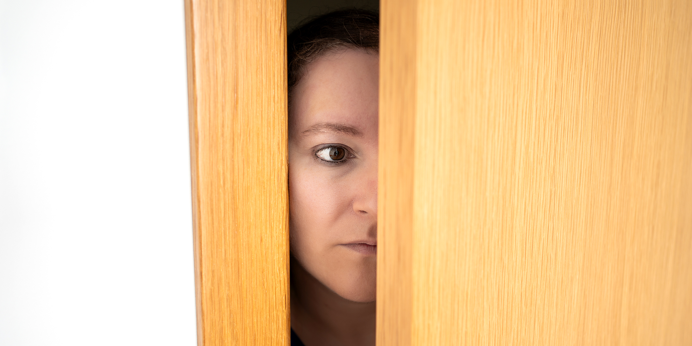 A startled woman eavesdropping from behind a door | Source: Shutterstock