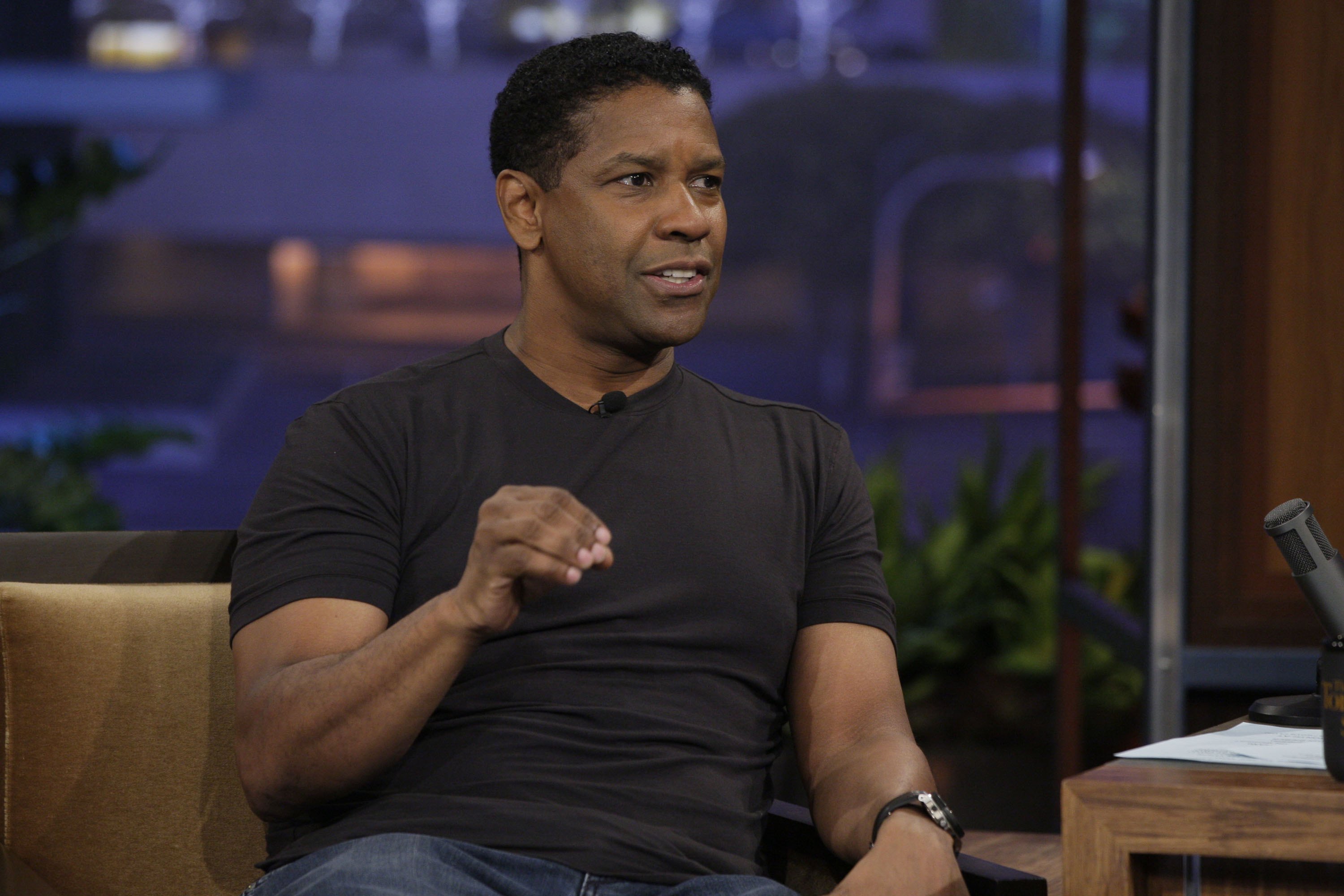 During an interview on "The Tonight Show," Denzel Washington appears in a fitted black tee, wearing his hair short and naturally wavy. His style is casual but polished, reflecting his confidence during a string of box-office successes.