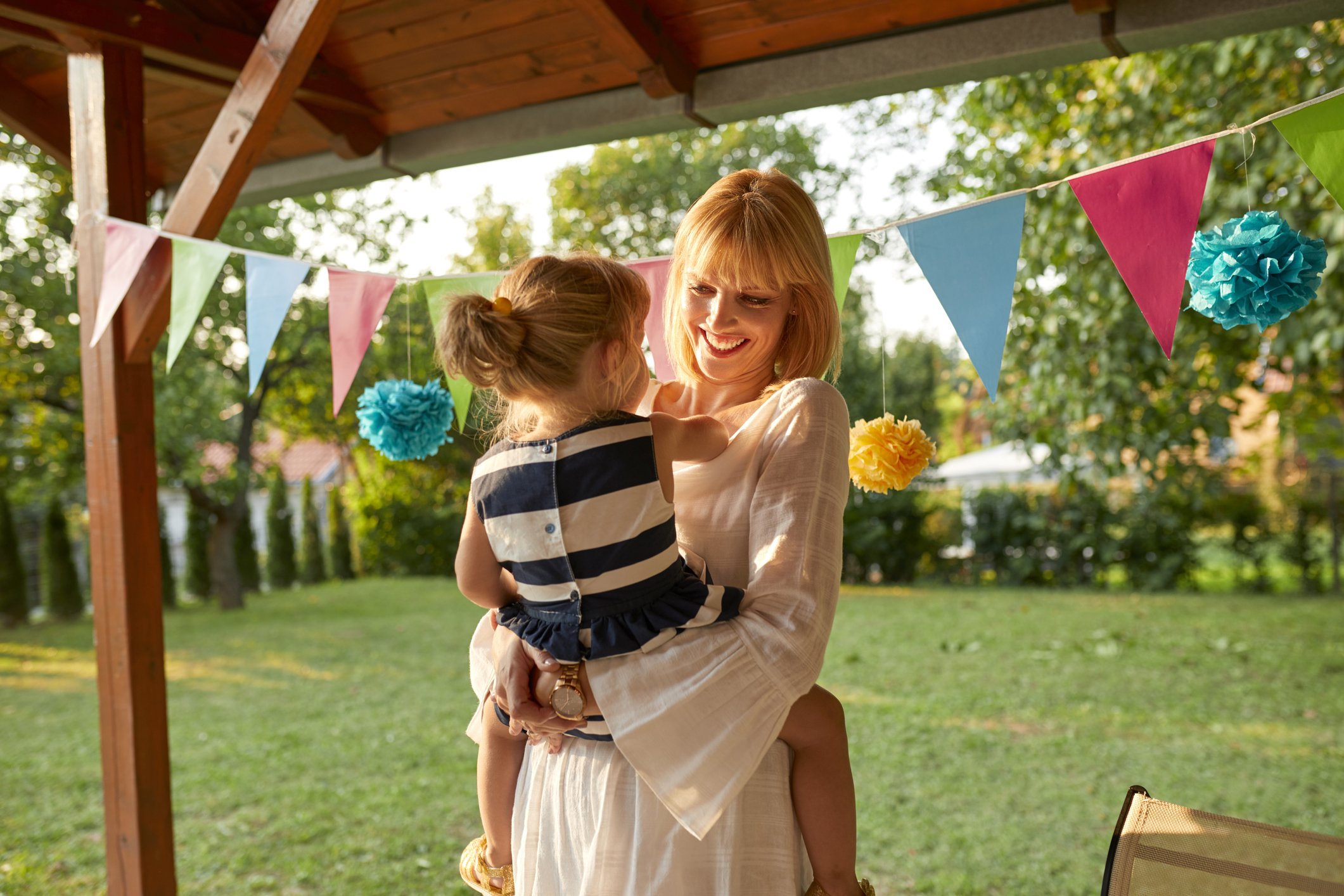 Glückliche Mutter, die ihre Tochter auf einer Gartengeburtstagsfeier trägt | Quelle: Getty Images