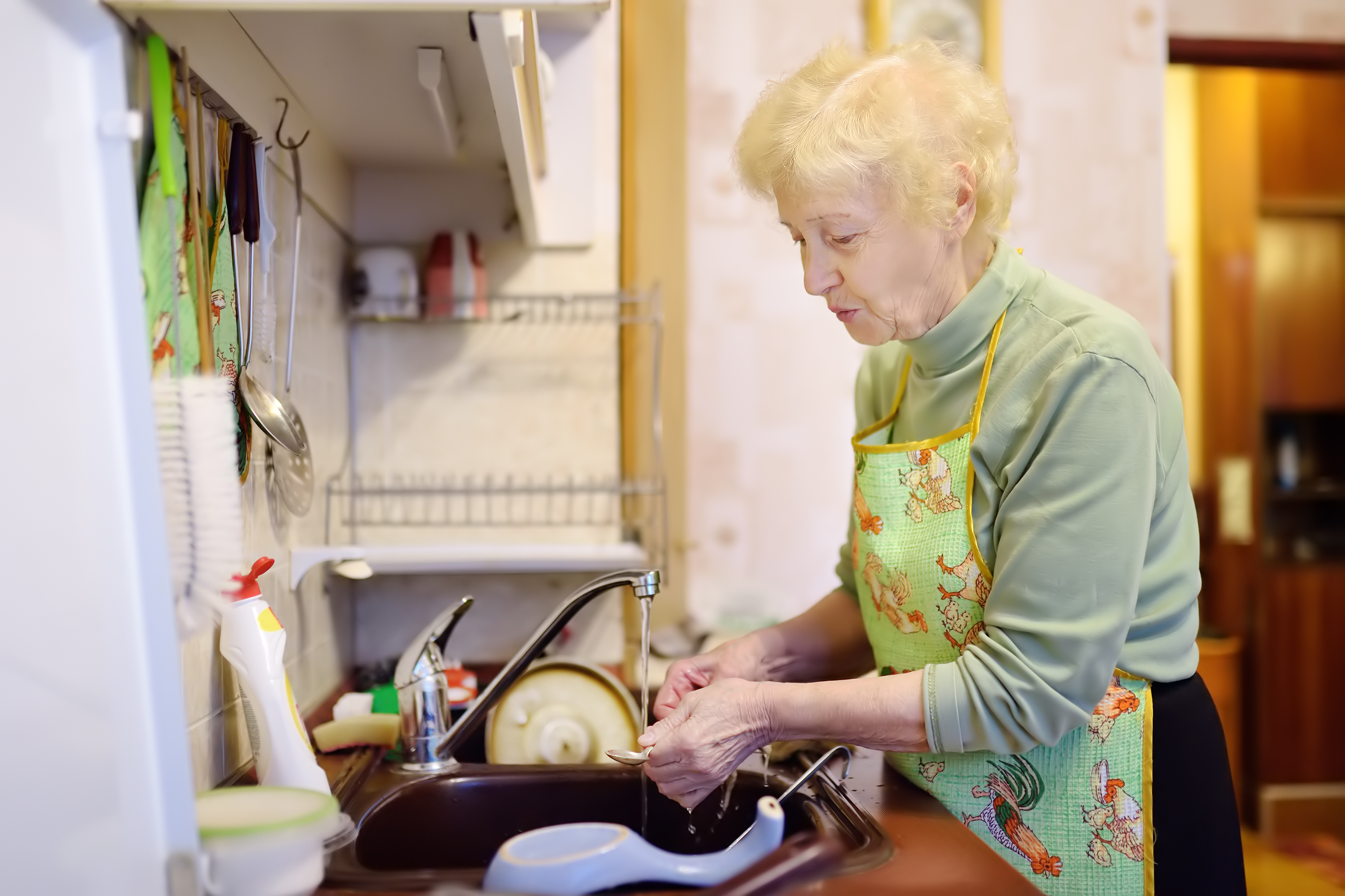 An elderly lady is washing dishes in the kitchen | Source: Shutterstock