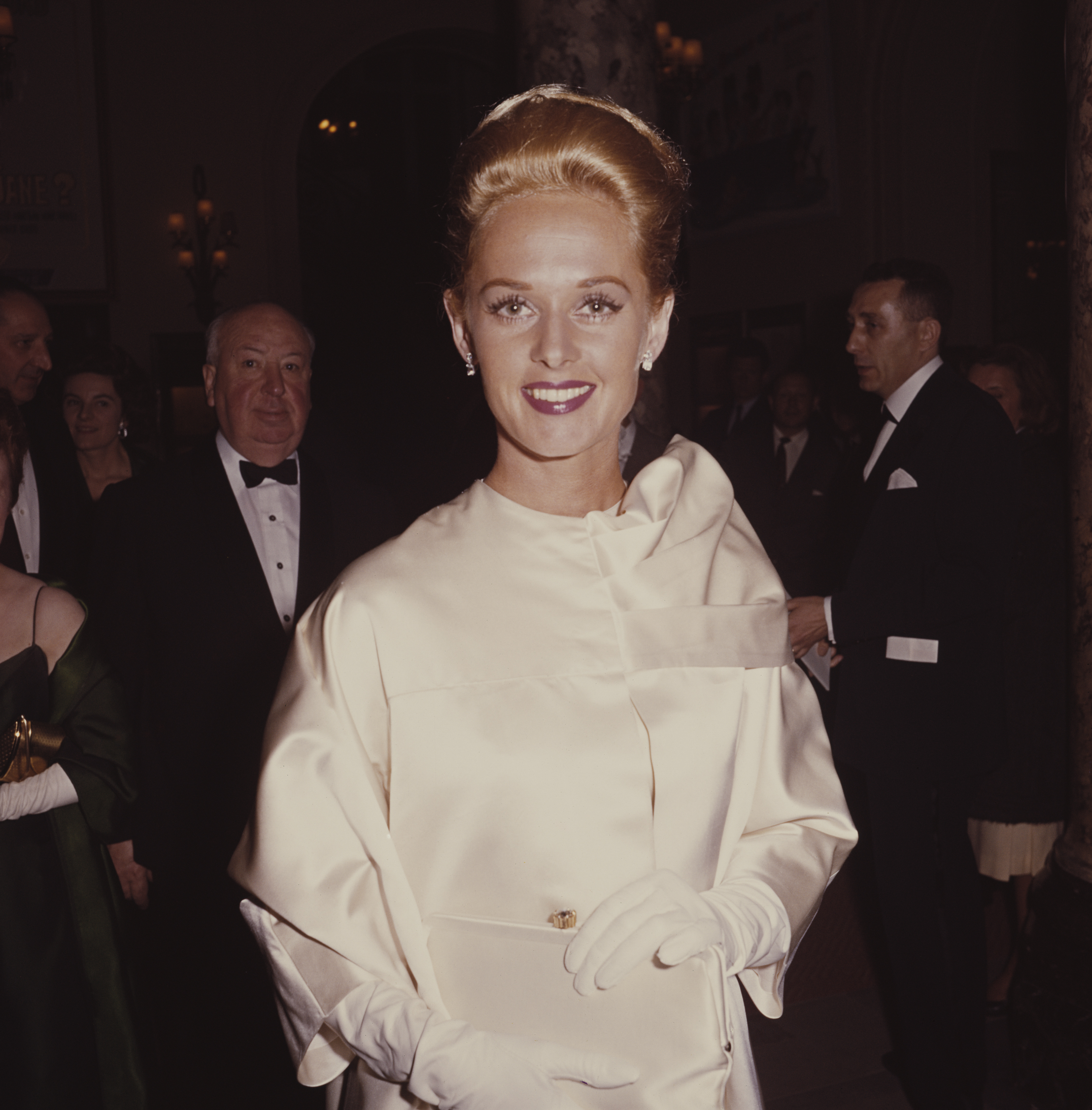 Tippi Hedren posed wearing a white silk style dress with matching white gloves at the Cannes film festival in France in May 1963. Behind her is the film director Alfred Hitchcock who directed Hedren in the film 'The Birds' | Source: Getty Images