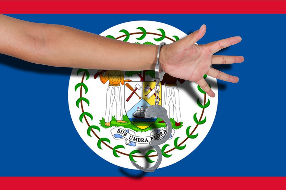 A photo of Handcuffs with hand on Belize flag | Photo: Shutterstock