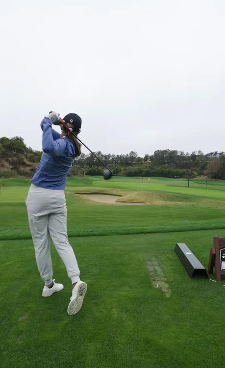 Kai Trump finishes her swing on the golf course, wearing a blue top, white pants, and a black cap on an overcast day | Source: Tiktok/thekaitrumpgolfer