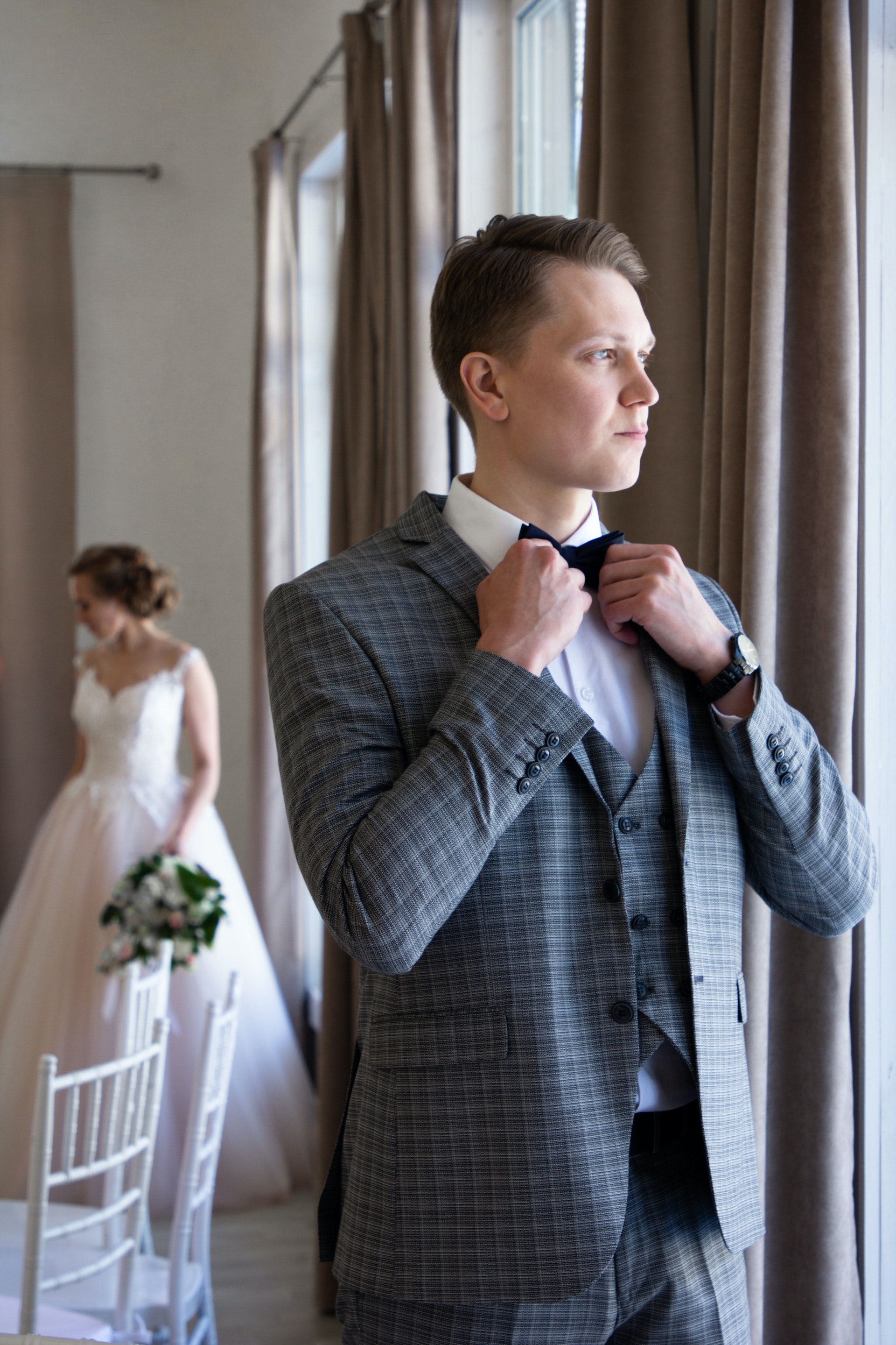 A groom looking outside a window with his bride standing in the background | Source: Pexels
