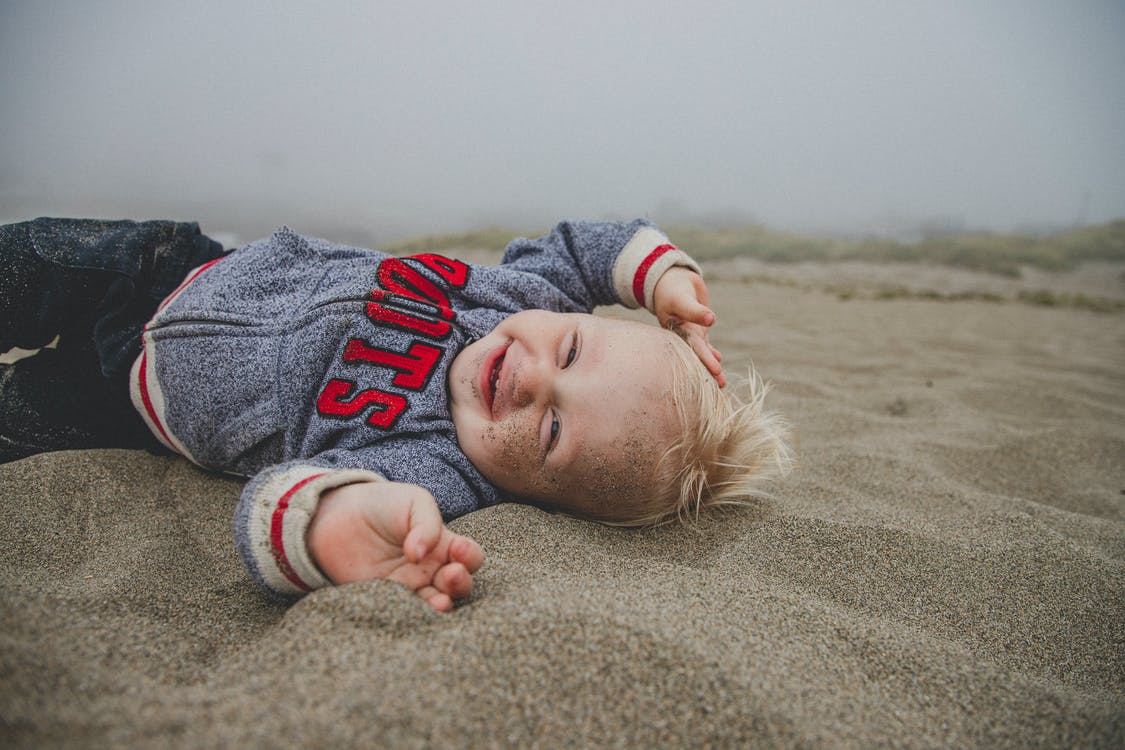 Un bebé sonriendo recostado sobre la arena. | Foto: Pexels