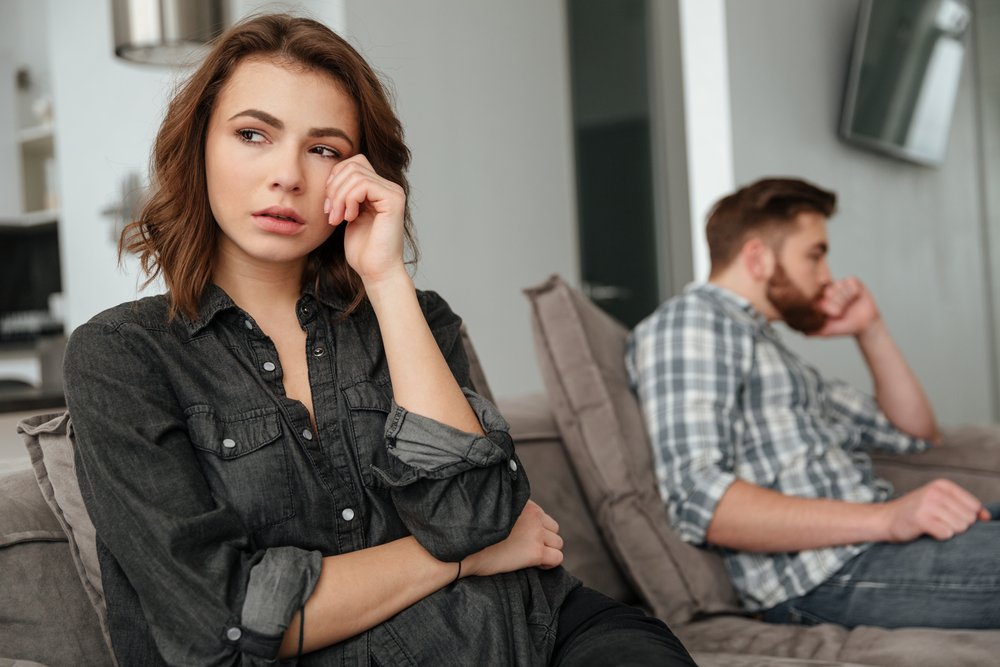 A photo of young sad couple sitting on sofa indoors. | Photo: Shutterstock