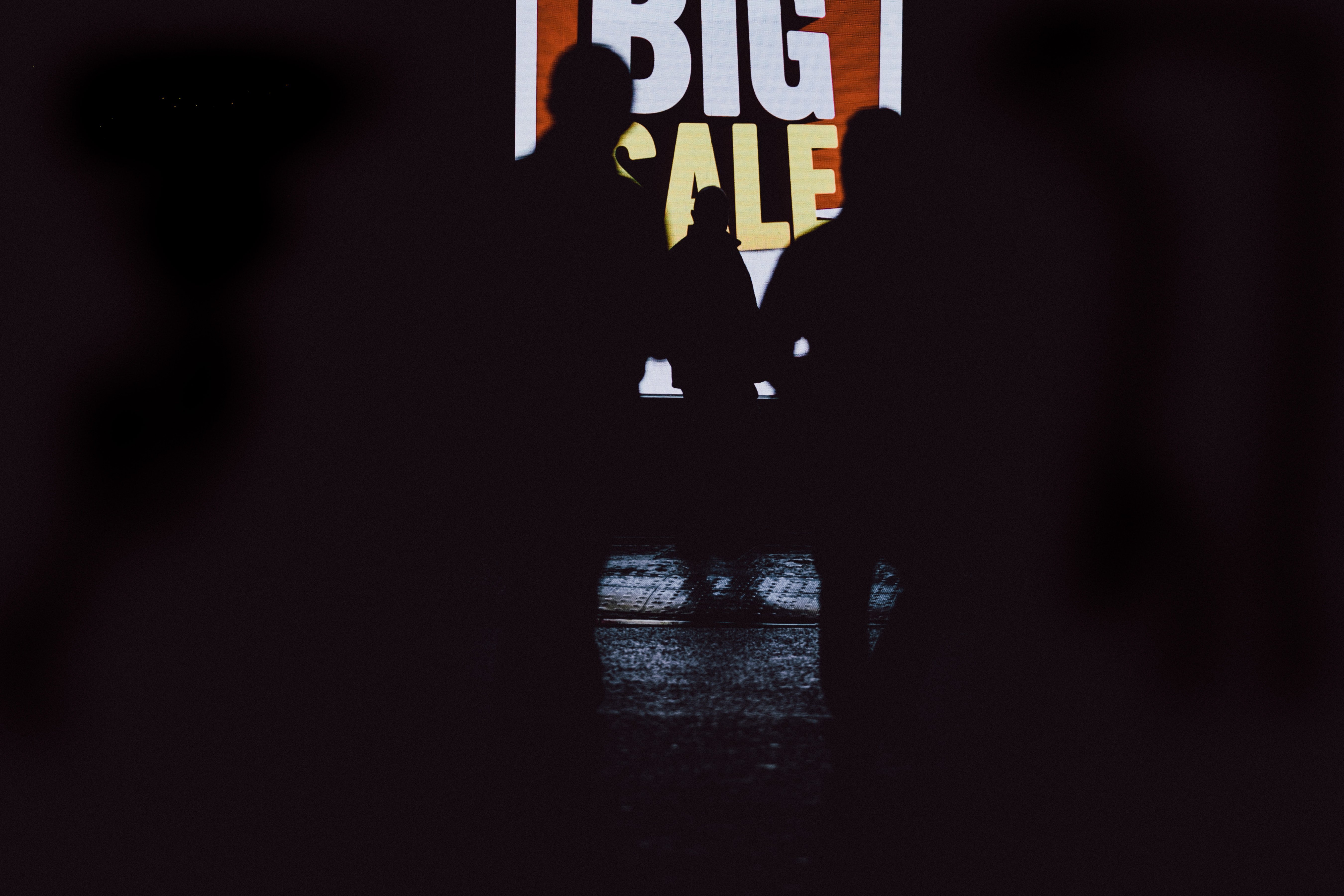 Silhouettes of people in front of a sale sign. | Source: Unsplash