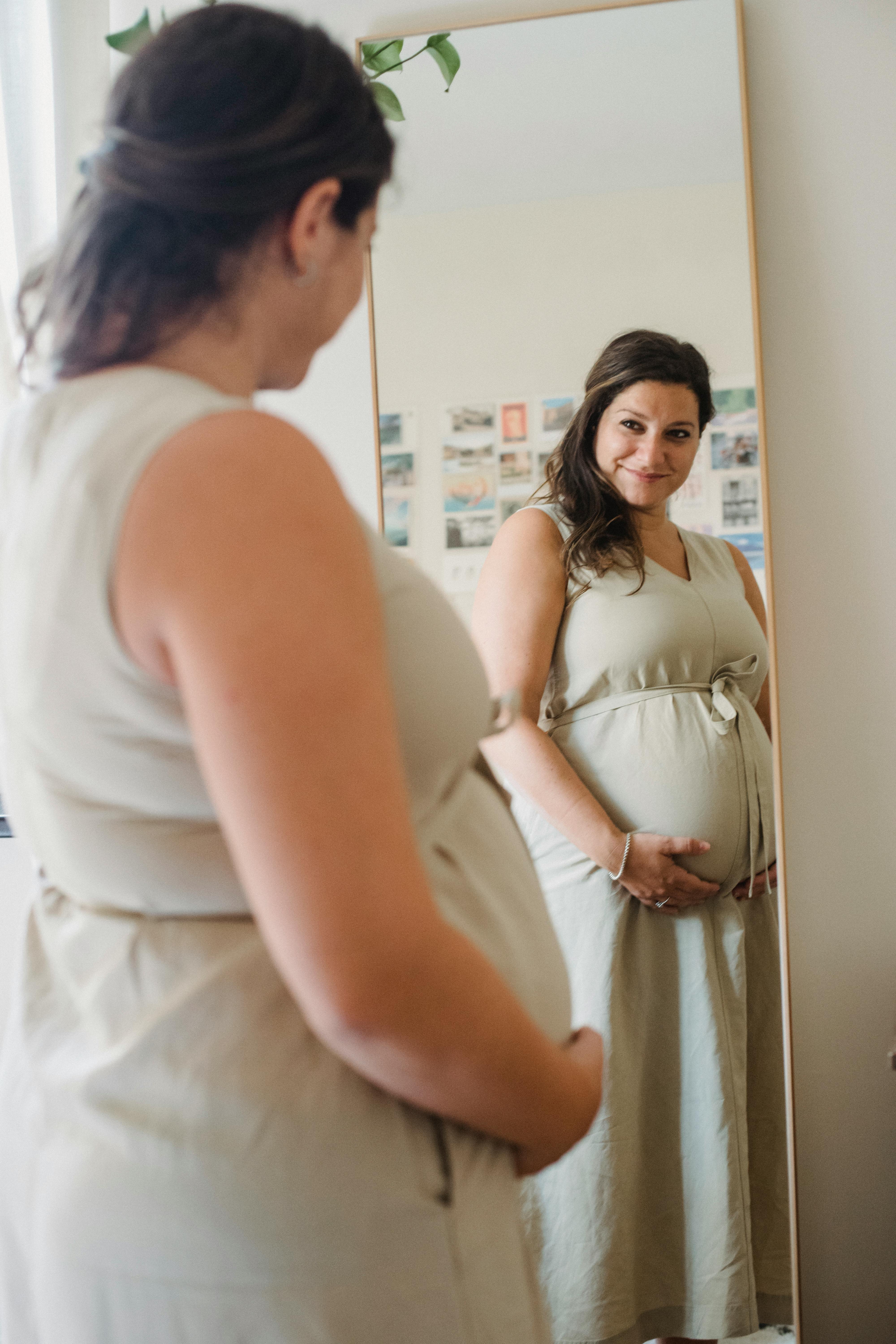 A happy pregnant woman looking at herself in a mirror | Source: Pexels