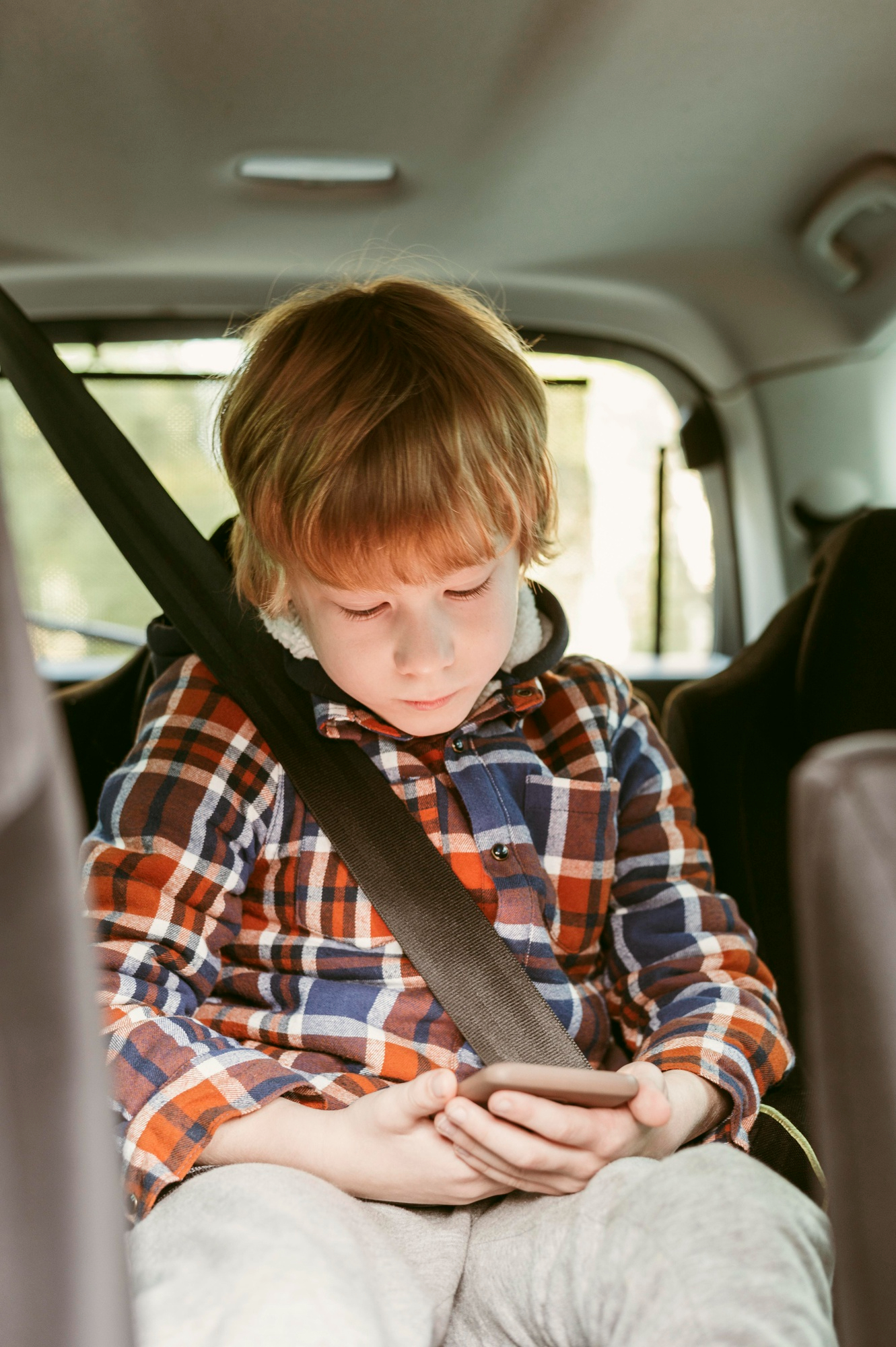 A little boy focused on a phone in the backseat of a car | Source: Freepik
