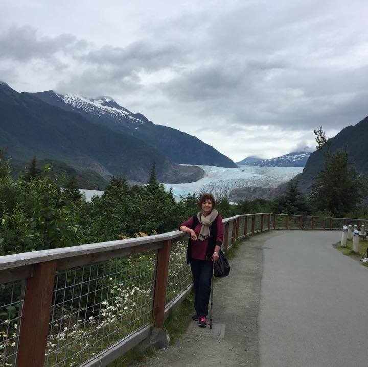 Nancy Guthrie stands on a paved walkway with a wooden-and-wire railing, set against a dramatic natural landscape, from a post dated August 30, 2019. | Facebook/NancyGuthrie