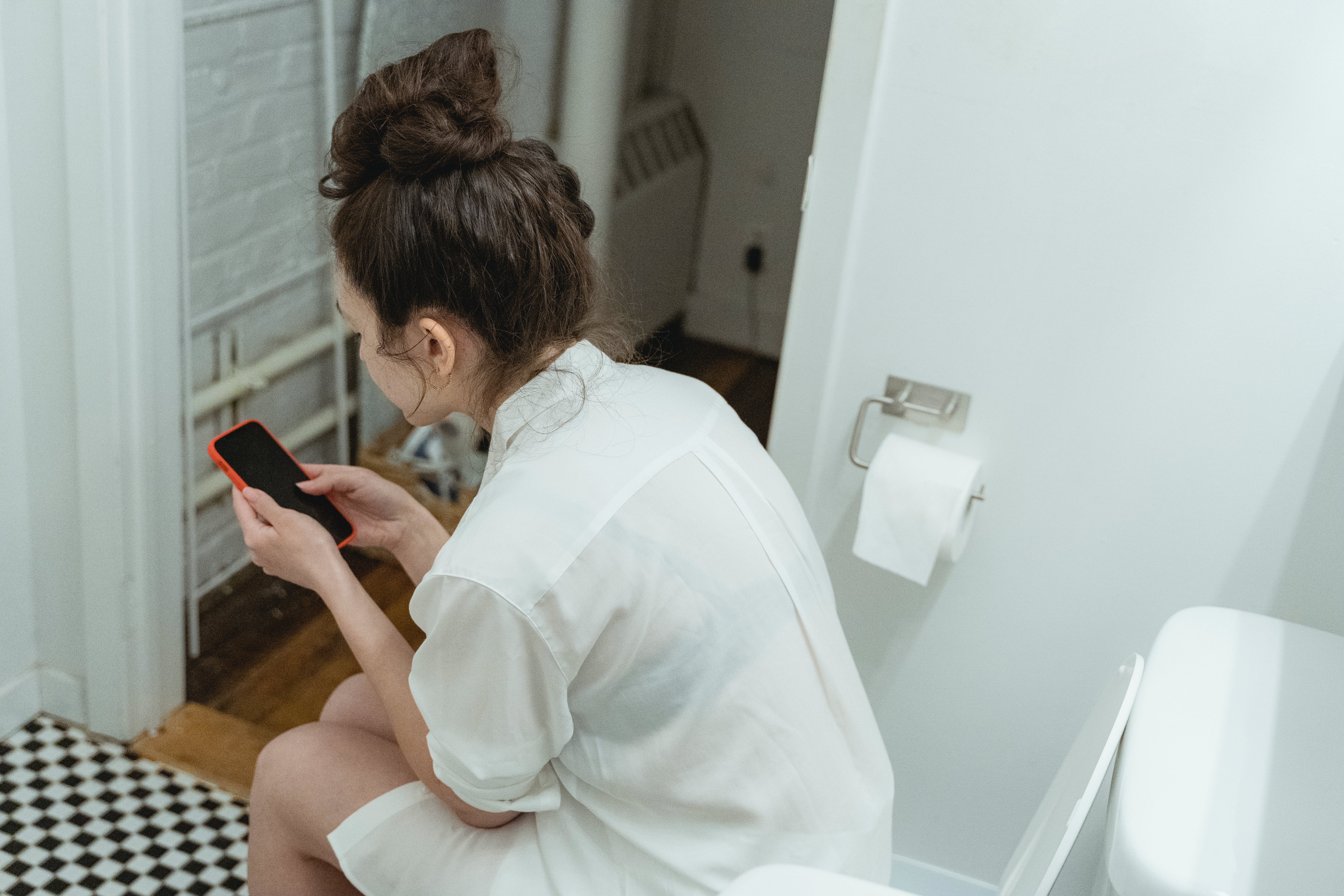 A woman sitting on a toilet while using her phone | Source: Pexels