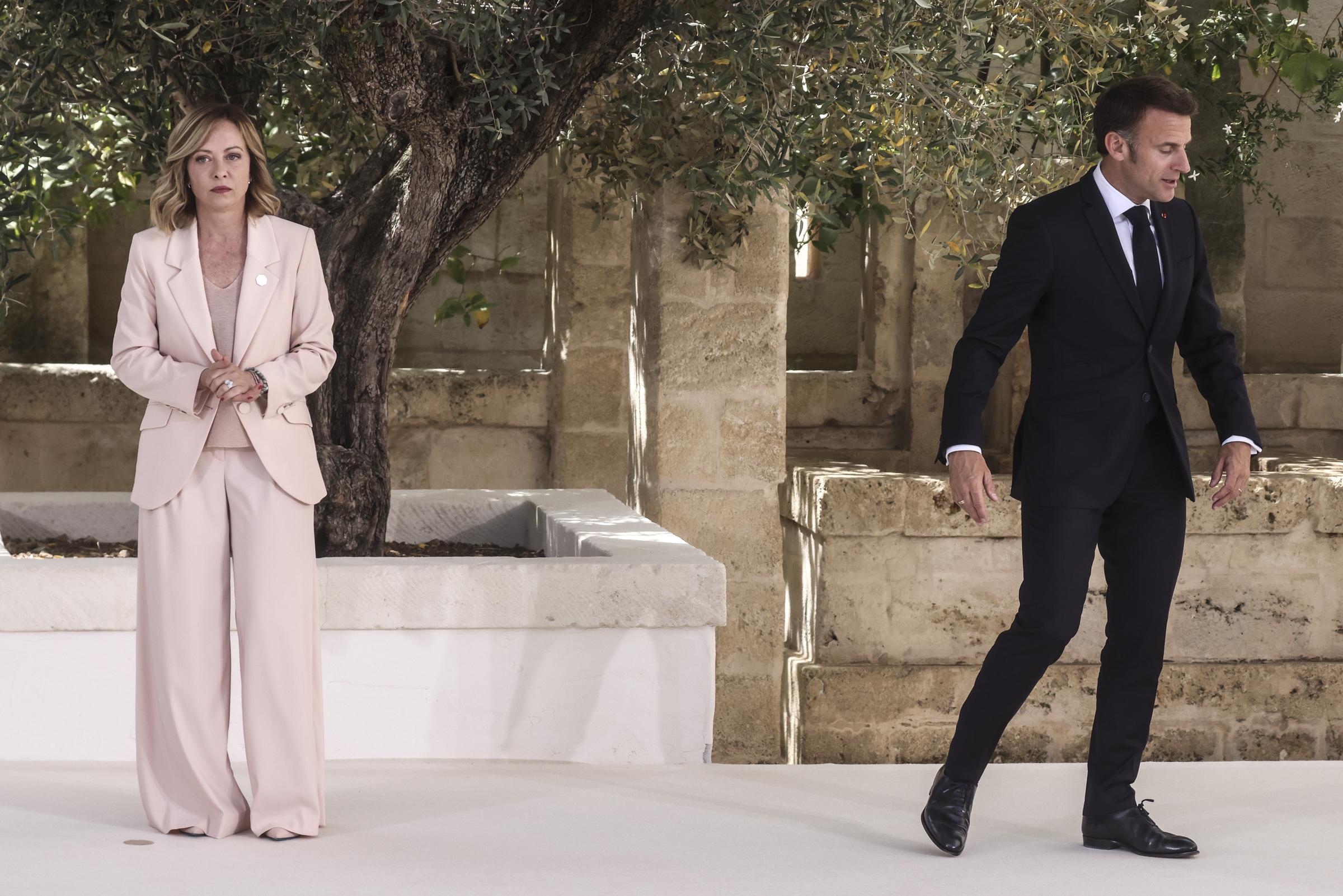 Emmanuel Macron walks away from Giorgia Meloni at Borgo Egnazia resort, where she stands waiting with her hands clasped.
