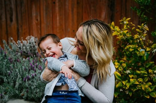 A woman playing with a young boy as she tickles him | Source: Unsplash