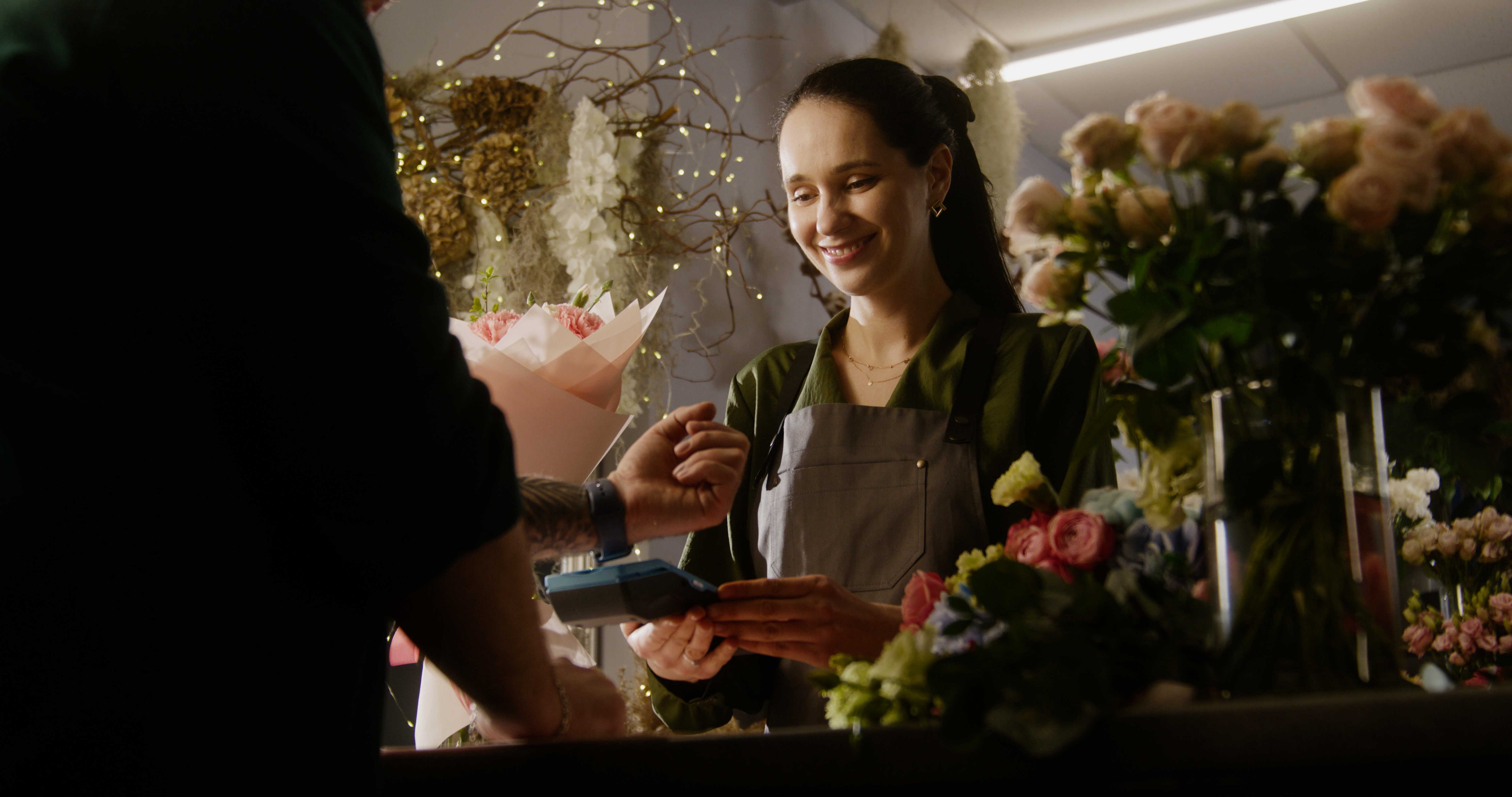 Man buys spring bouquet in flower shop and pays for purchase with contactless payment using smart watch. | Source: Shutterstock