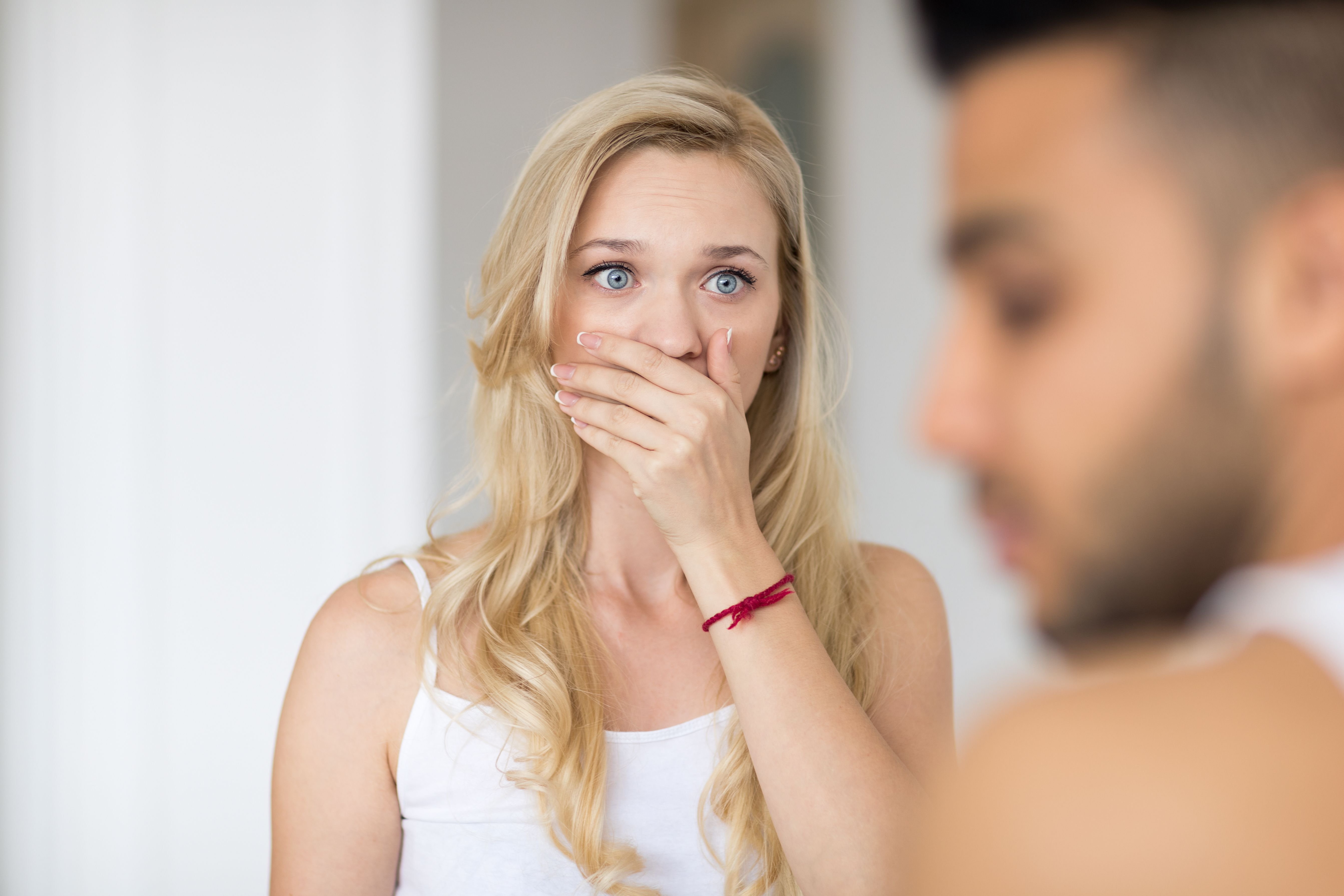 Blonde woman with blue eyes covers her mouth with one hand looking at man with shock in her eyes | Photo: Shutterstock