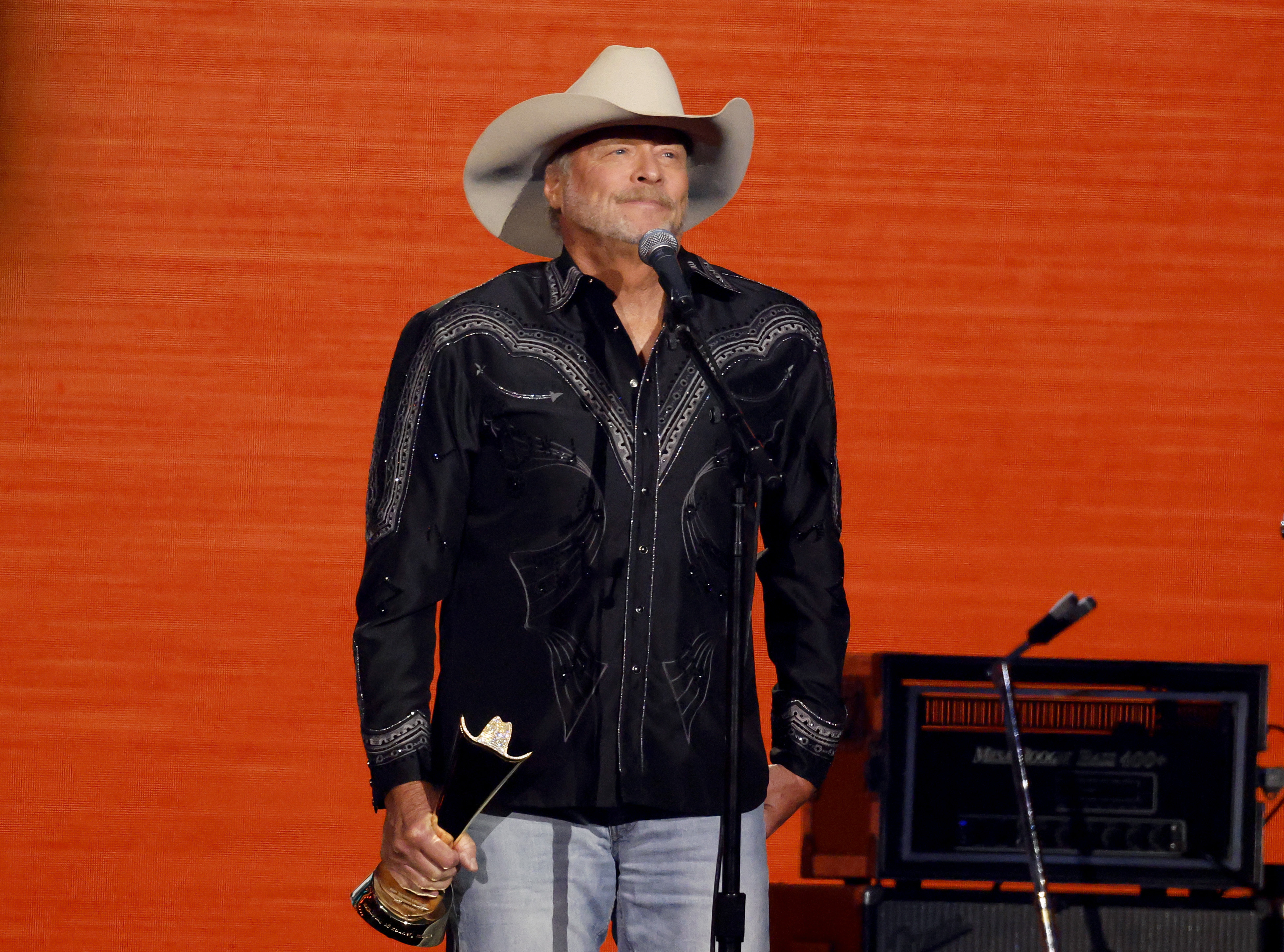 Alan Jackson accepts the ACM Alan Jackson Lifetime Achievement Award onstage during the 60th ACM Awards. Wearing a black embroidered western shirt and cowboy hat, Jackson holds his award while addressing the audience.