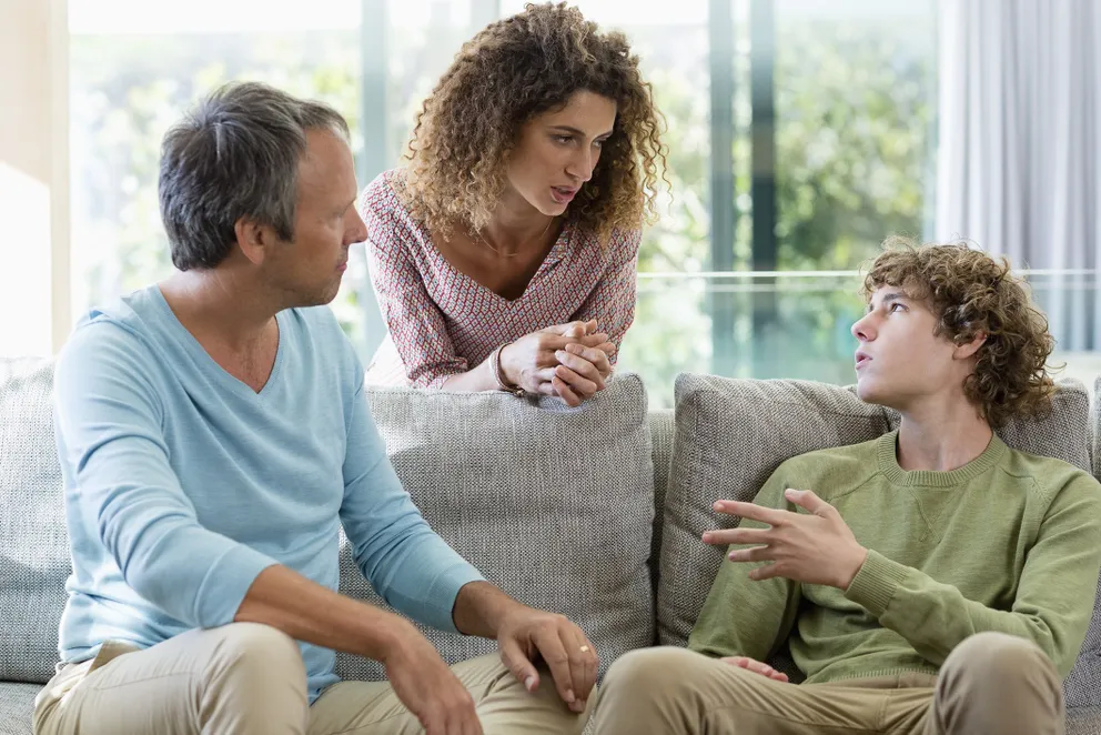 Les parents parlent à leur fils adolescent dans le salon | Photo : Getty Images
