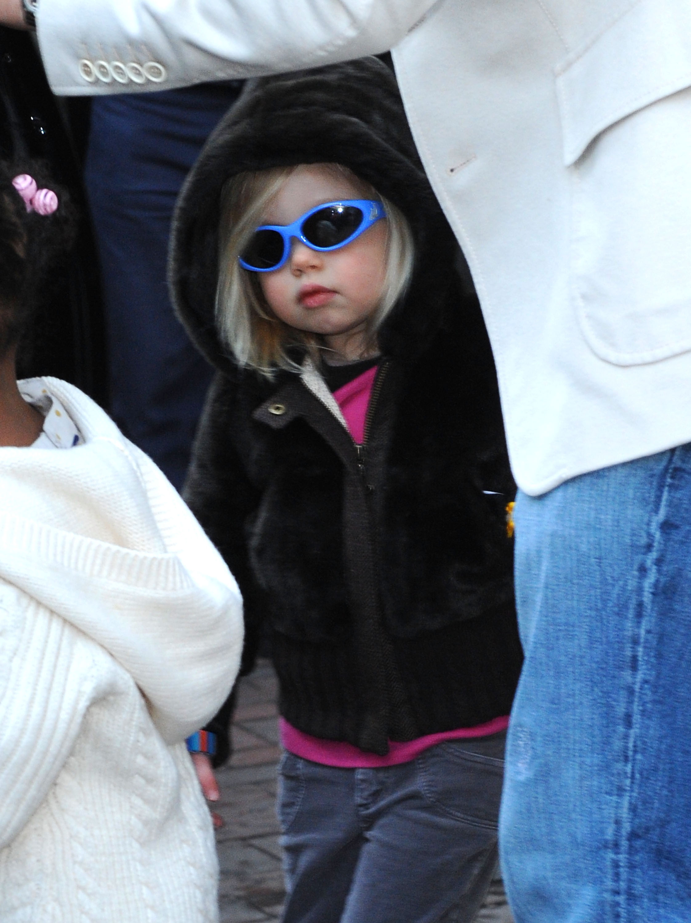 Shiloh Jolie-Pitt steps out in Washington, DC, wearing a dark hooded jacket and bold blue sunglasses. Walking beside her siblings, her playful yet self-assured style stands out even at a young age. The look hints early on at the individuality that would later define her evolution.