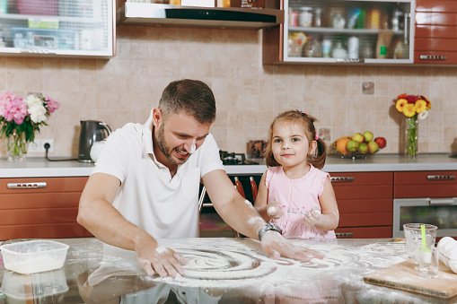 Photo of little kid and her dad drawing on scattered flour on kitchen table | Photo: Getty Images