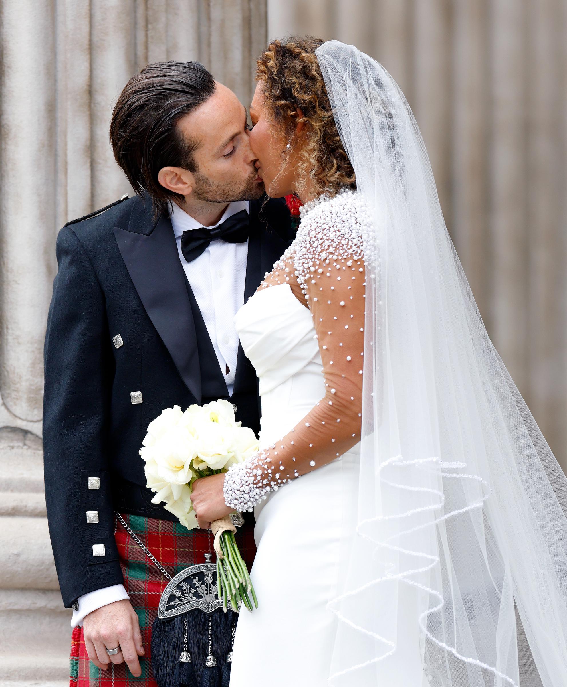 Mel B and Rory McPhee share a tender, passionate kiss. The intimacy of the moment is unmistakable—eyes closed, expressions soft, and the world around them seemingly paused as they savor their first moments as husband and wife.