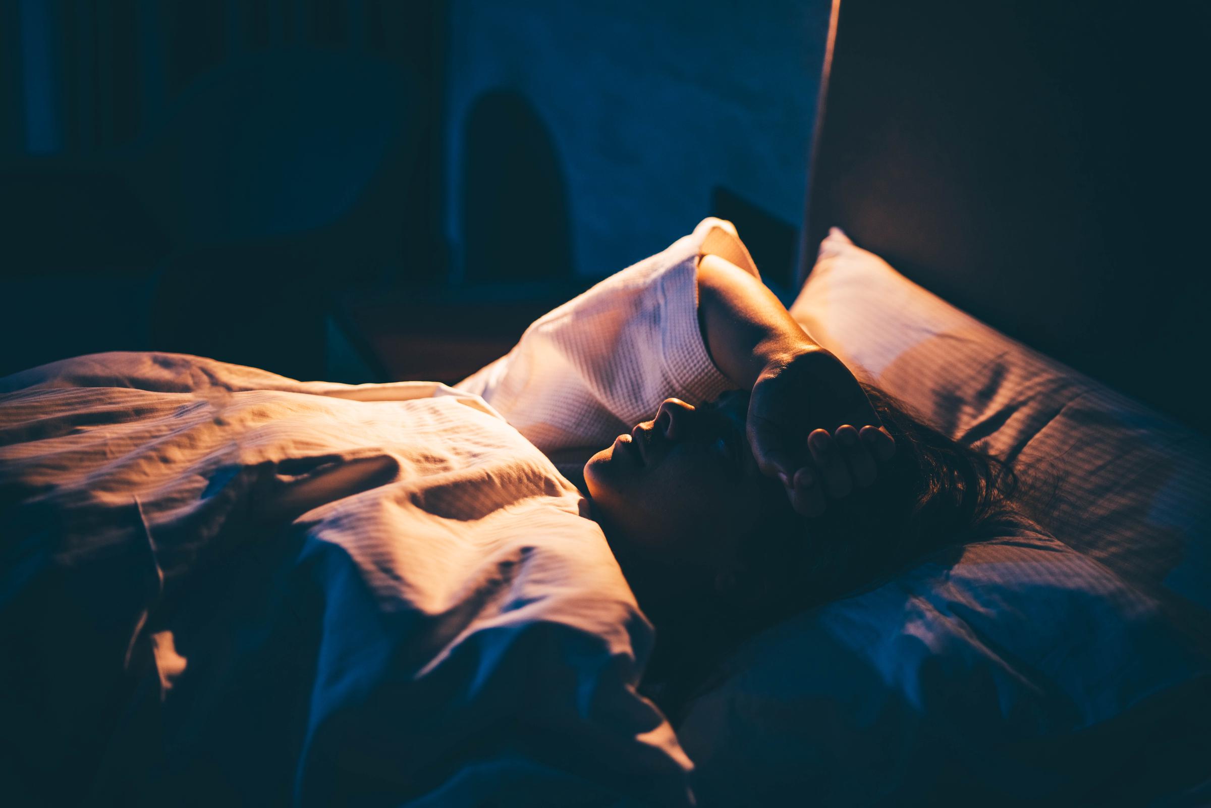 Young woman struggling with insomnia, lying in bed with her hand on her forehead | Source: Getty Images