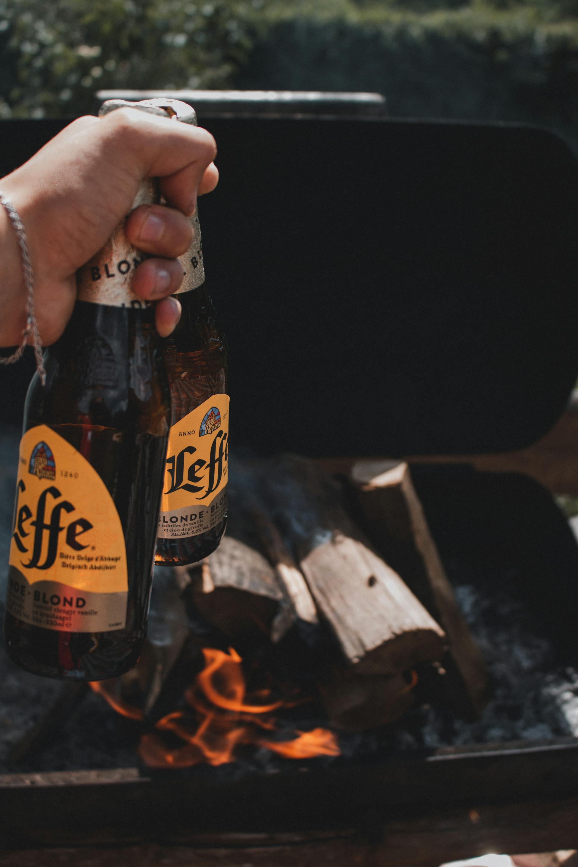 A person holding beer with firewood in the background | Source: Pexels