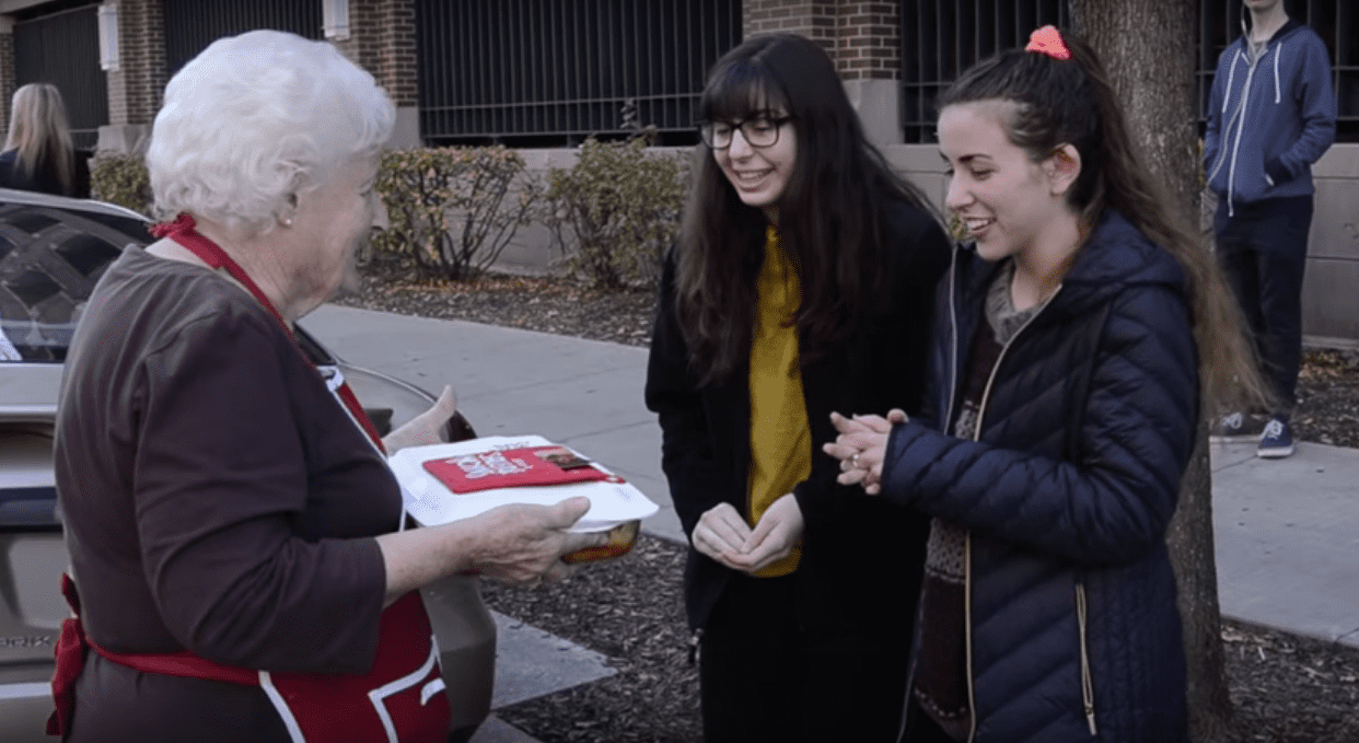 Une "Sausage Nonna" présente un repas à 2 jeunes femmes en pleine rue. | YouTube/officiel Johnsonville