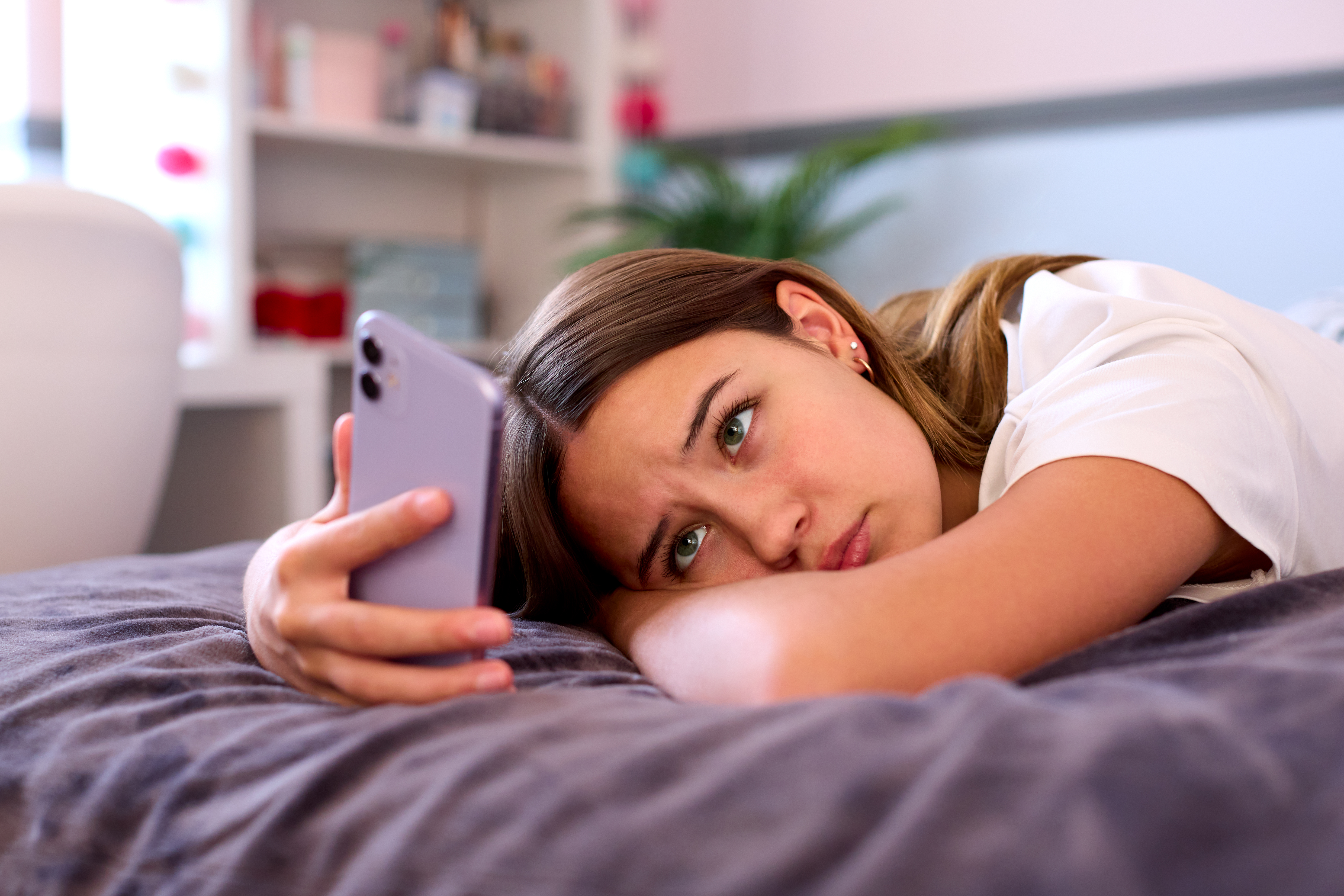 Depressed Teenage Girl Lying On Bed At Home Looking At Mobile Phone | Source: Getty Images
