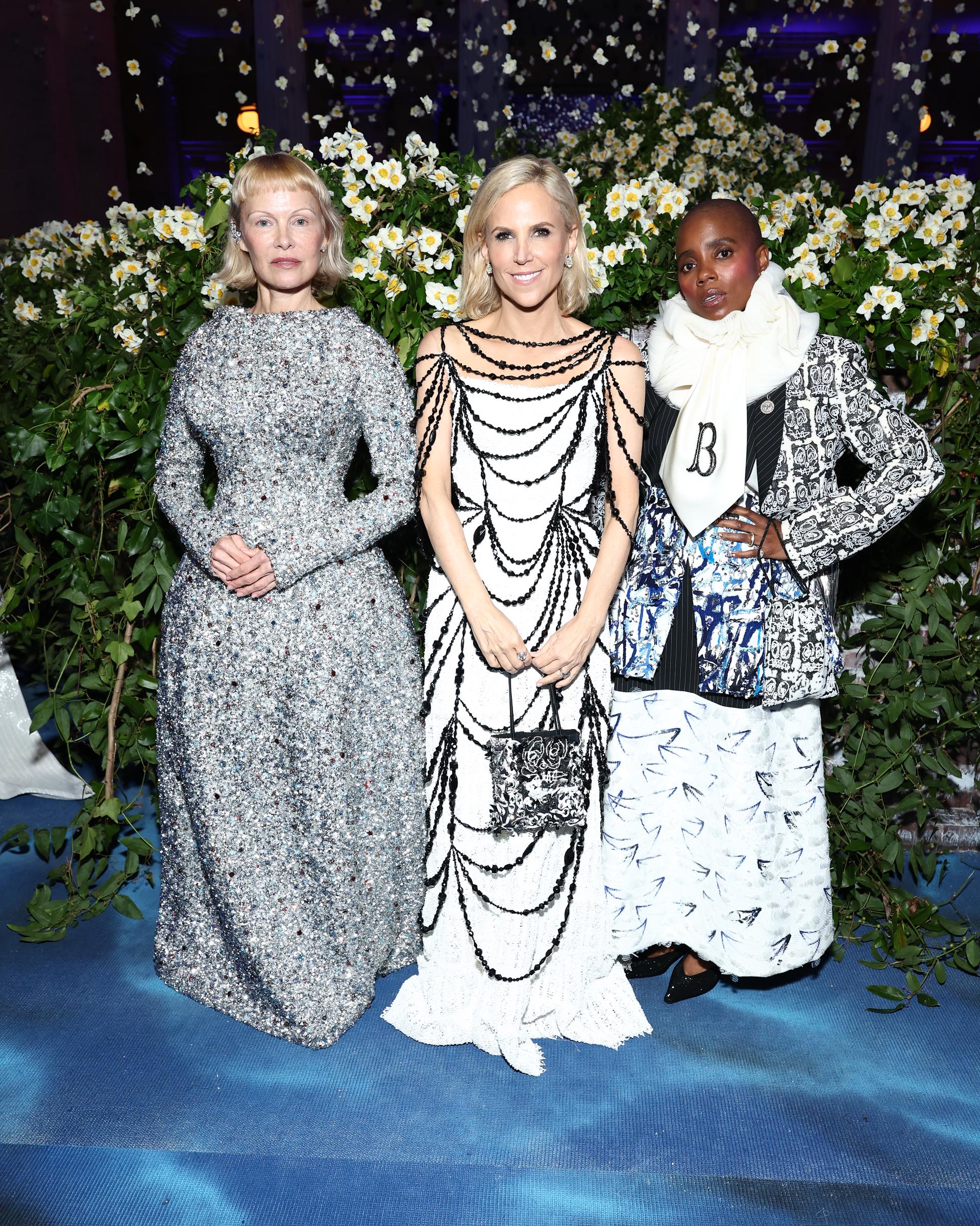 Pamela Anderson, Tory Burch, and Janicza Bravo are pictured at the Met Gala surrounded by floral displays. The trio's presence highlighted cross-industry creativity at the event honoring "Superfine: Tailoring Black Style" in New York City.