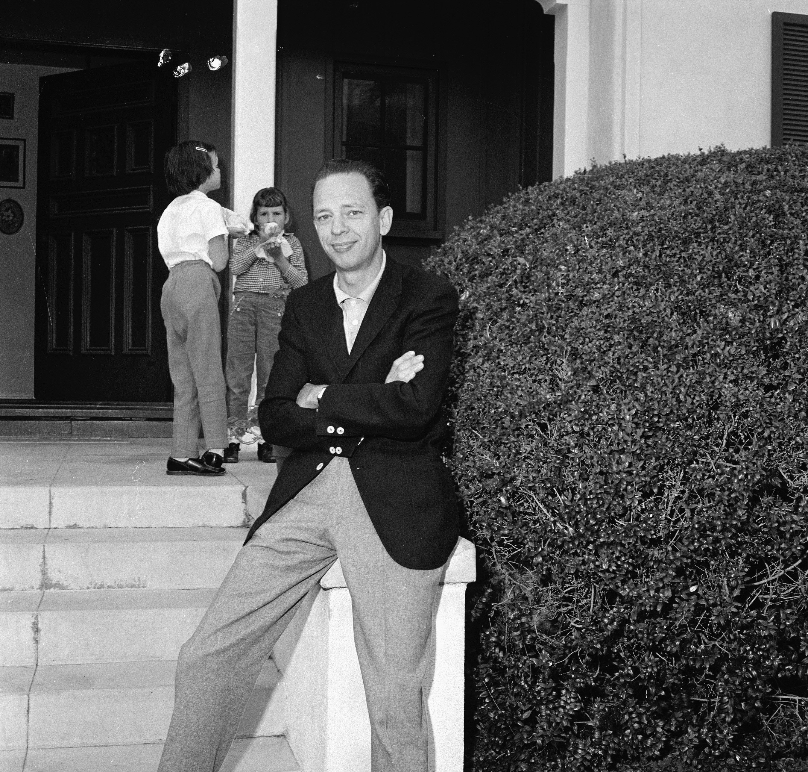 Portrait of American television actor Don Knotts as he poses, arms crossed, at the bottom of the steps to his house and his daughter Karen (in white) eats with a friend in the background.  March 2, 1961.| Source: Getty Images