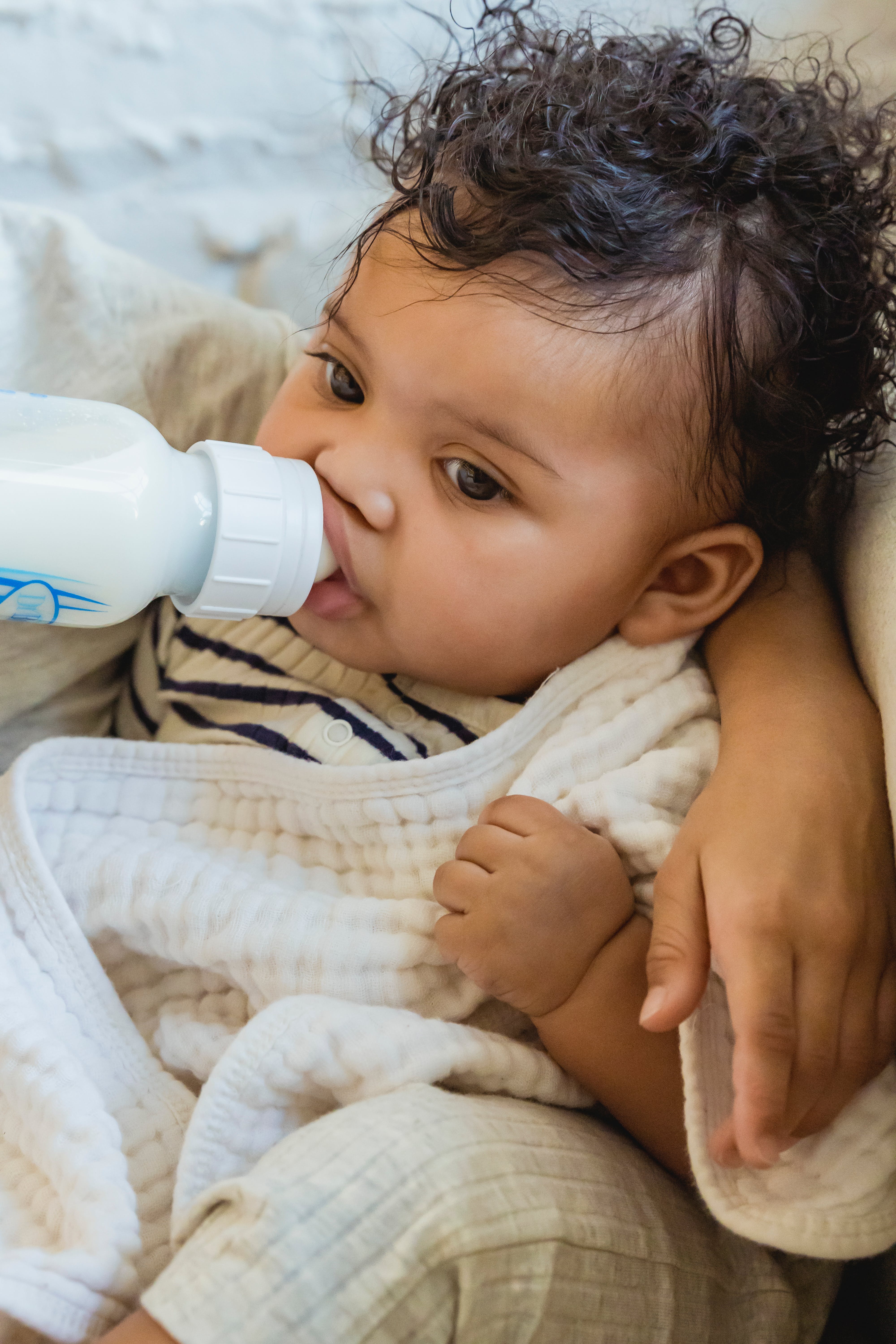 A baby suckling milk from a bottle while covered in a blanket | Source: Pexels