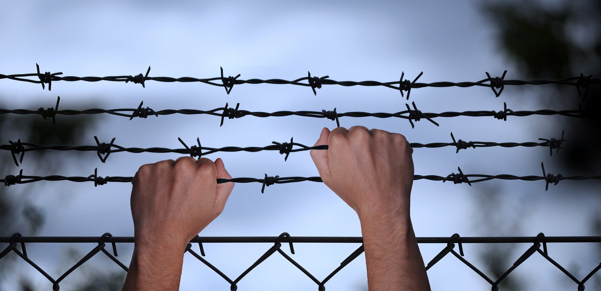Hands grabbing a barbed-wire fence. | Photo: Pixabay/Gerd Altmann