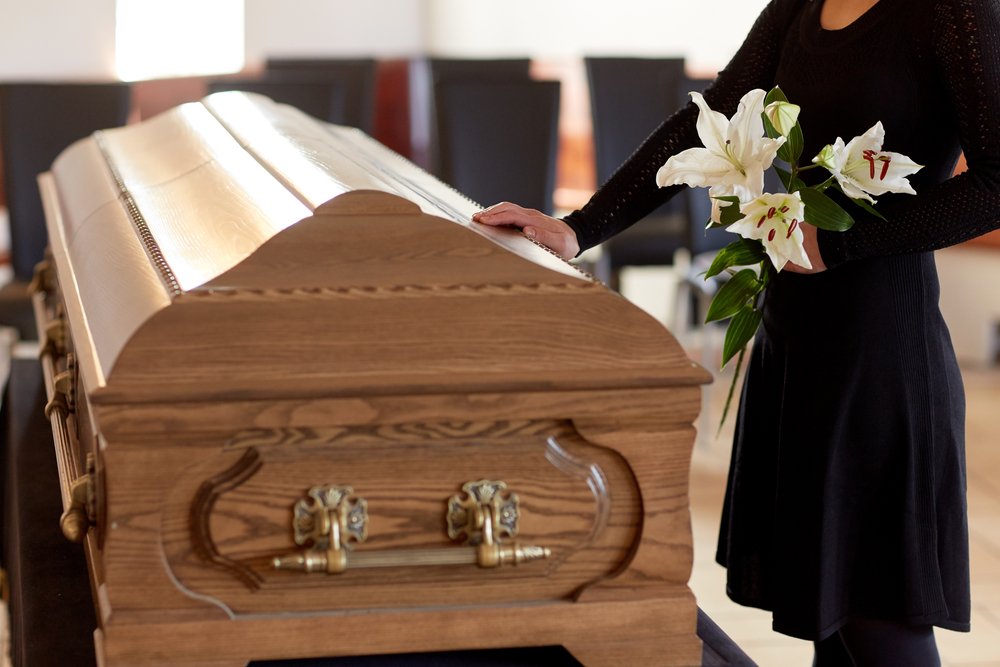 A woman with white lily flowers and hands on a coffin at funeral. | Photo: Shutterstock.