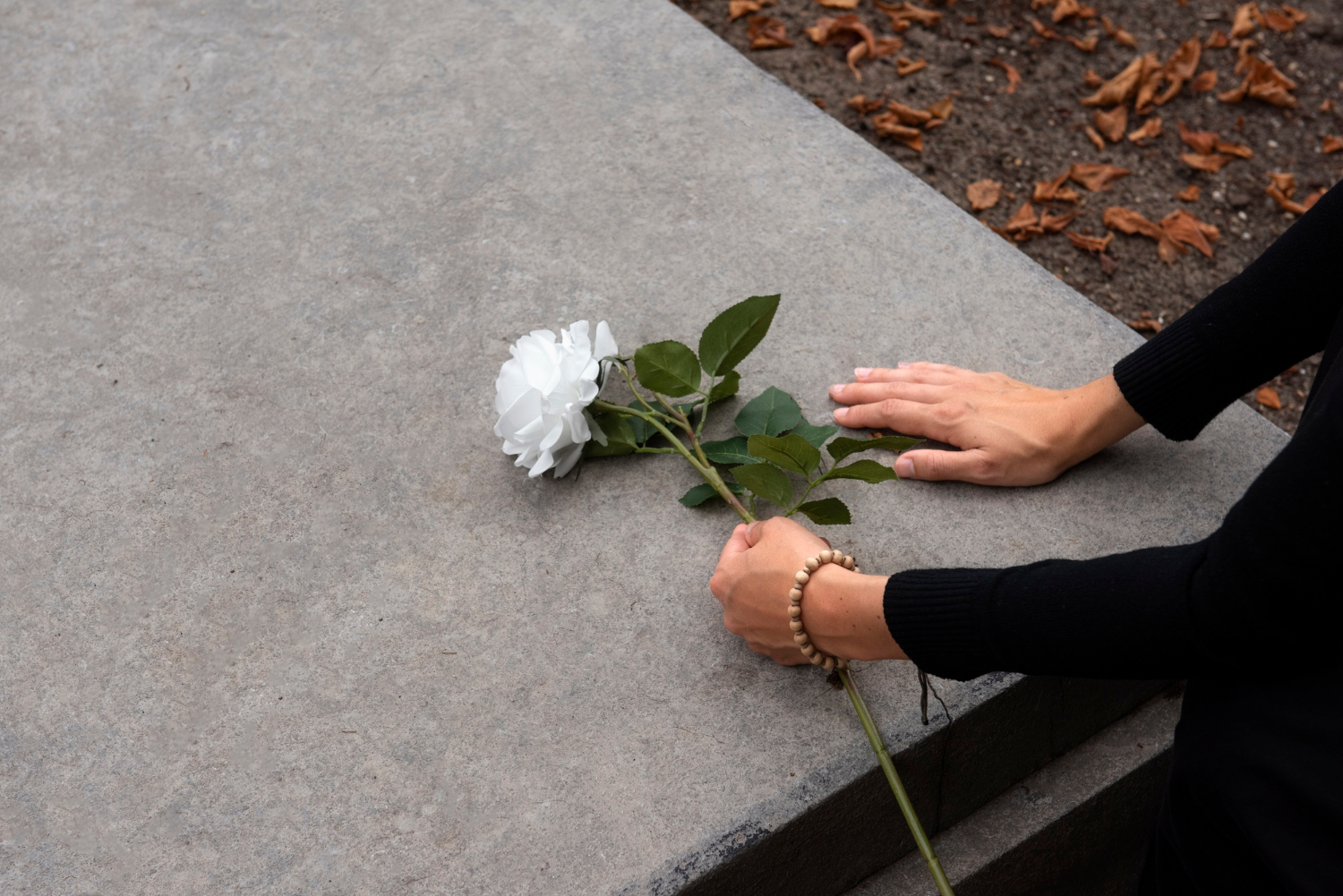 A woman placing a white rose on a gravestone | Source: Freepik