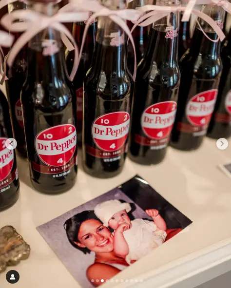 A charming display of Dr. Pepper bottles, decorated with pink ribbons, sat alongside a vintage photo of Ree and baby Alex, adding a nostalgic and sentimental touch to the celebration. The setup was a sweet nod to the Drummond family's cherished traditions. | Source: Instagram/ thepioneerwoman