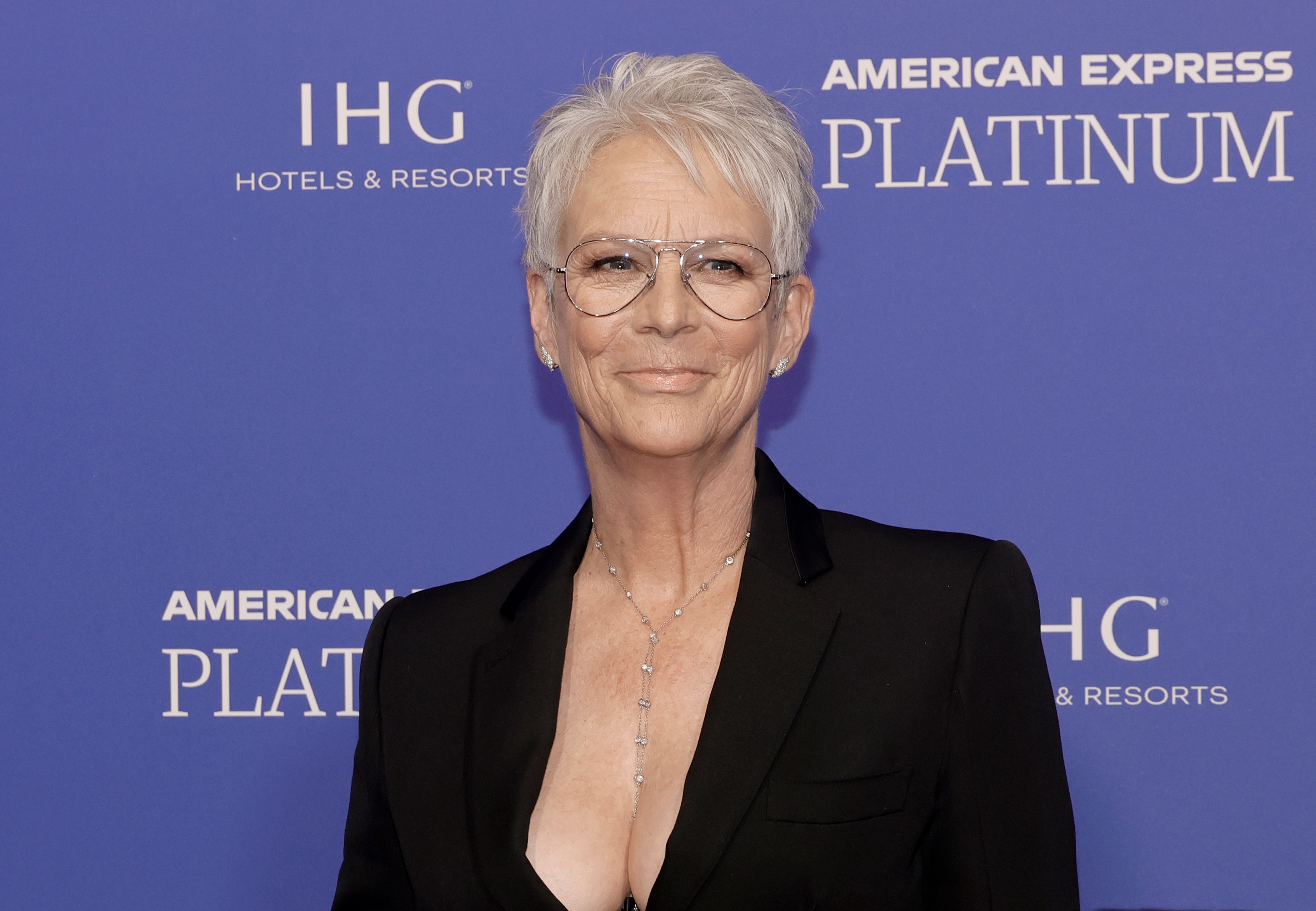 Jamie Lee Curtis stuns in a sleek black suit and plunging neckline at the 2023 Palm Springs International Film Festival Gala, accessorized with a delicate drop necklace and oversized glasses that framed her signature silver crop.