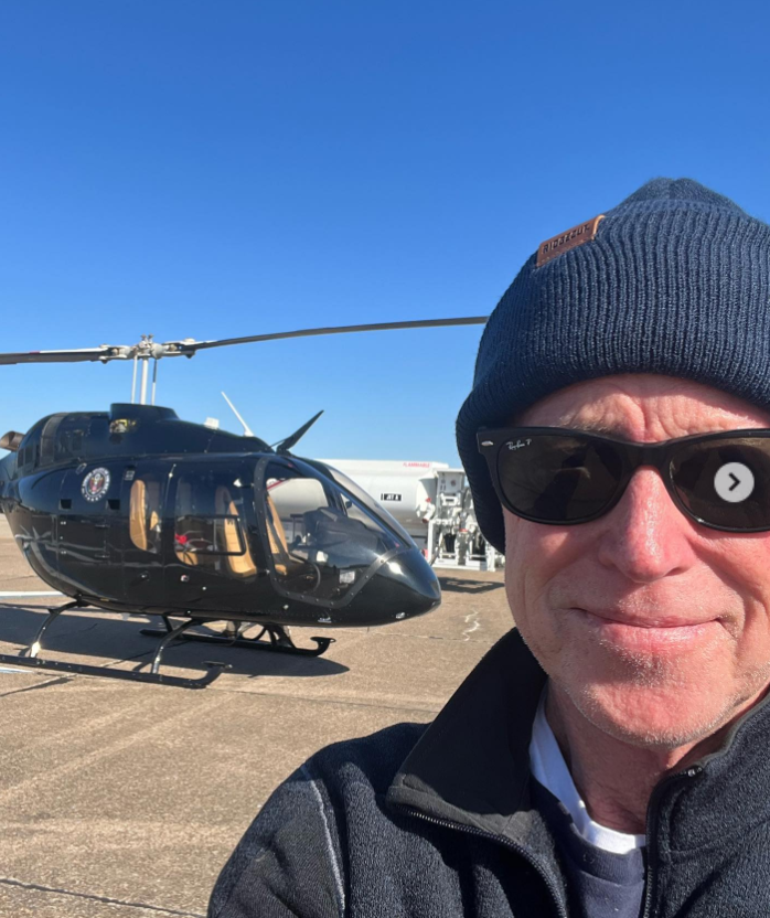 Mike Norris captures a windswept selfie on the tarmac, bundled in a beanie and sunglasses as a sleek black helicopter rests behind him. | Source: Instagram/iammikenorris
