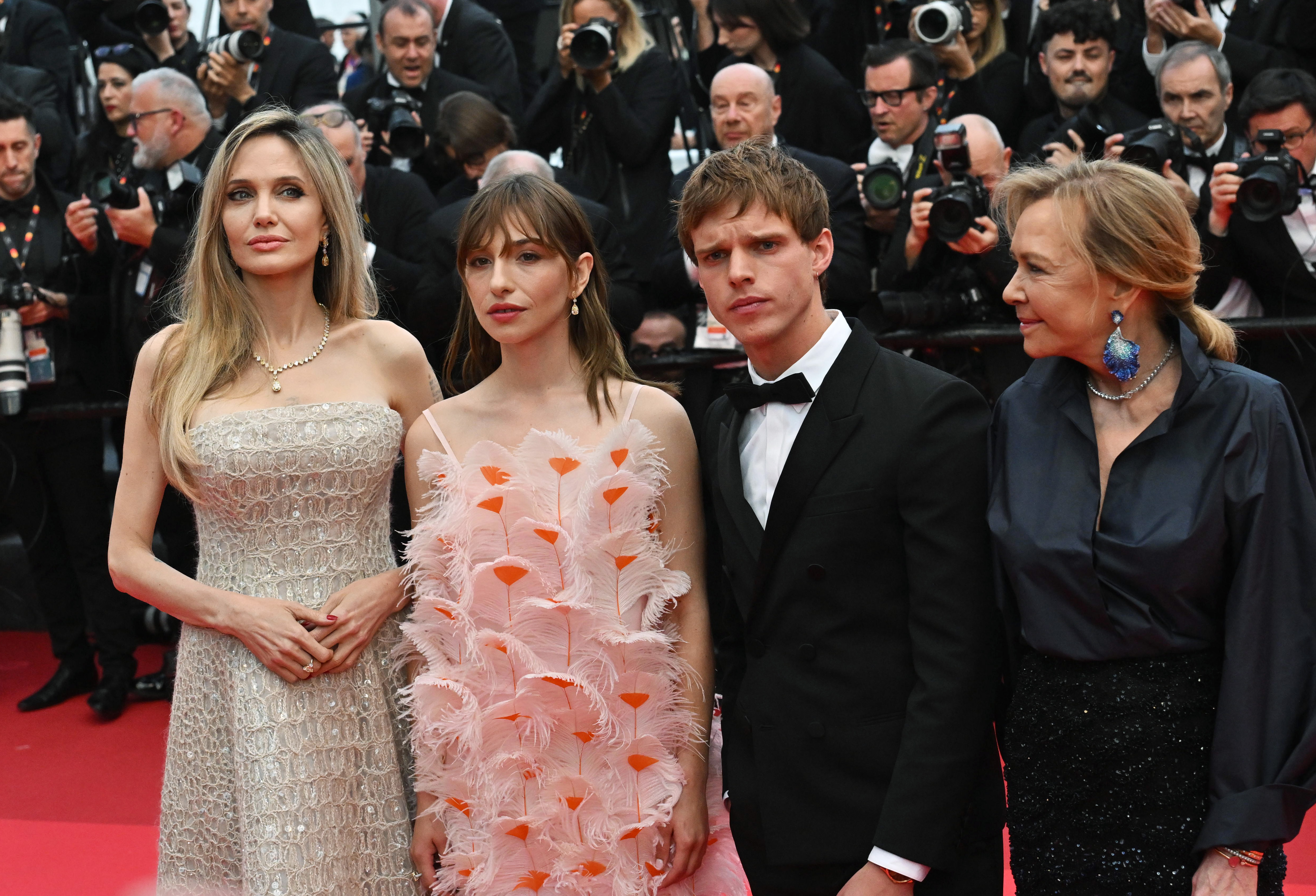 Angelina Jolie poses alongside Marie Colomb, Finn Bennett, and Caroline Scheufele at the premiere of "Eddington." Dressed in a sparkling champagne ball gown, Jolie brings refined glamour to the group portrait, flanked by co-stars and collaborators amid a storm of camera flashes.