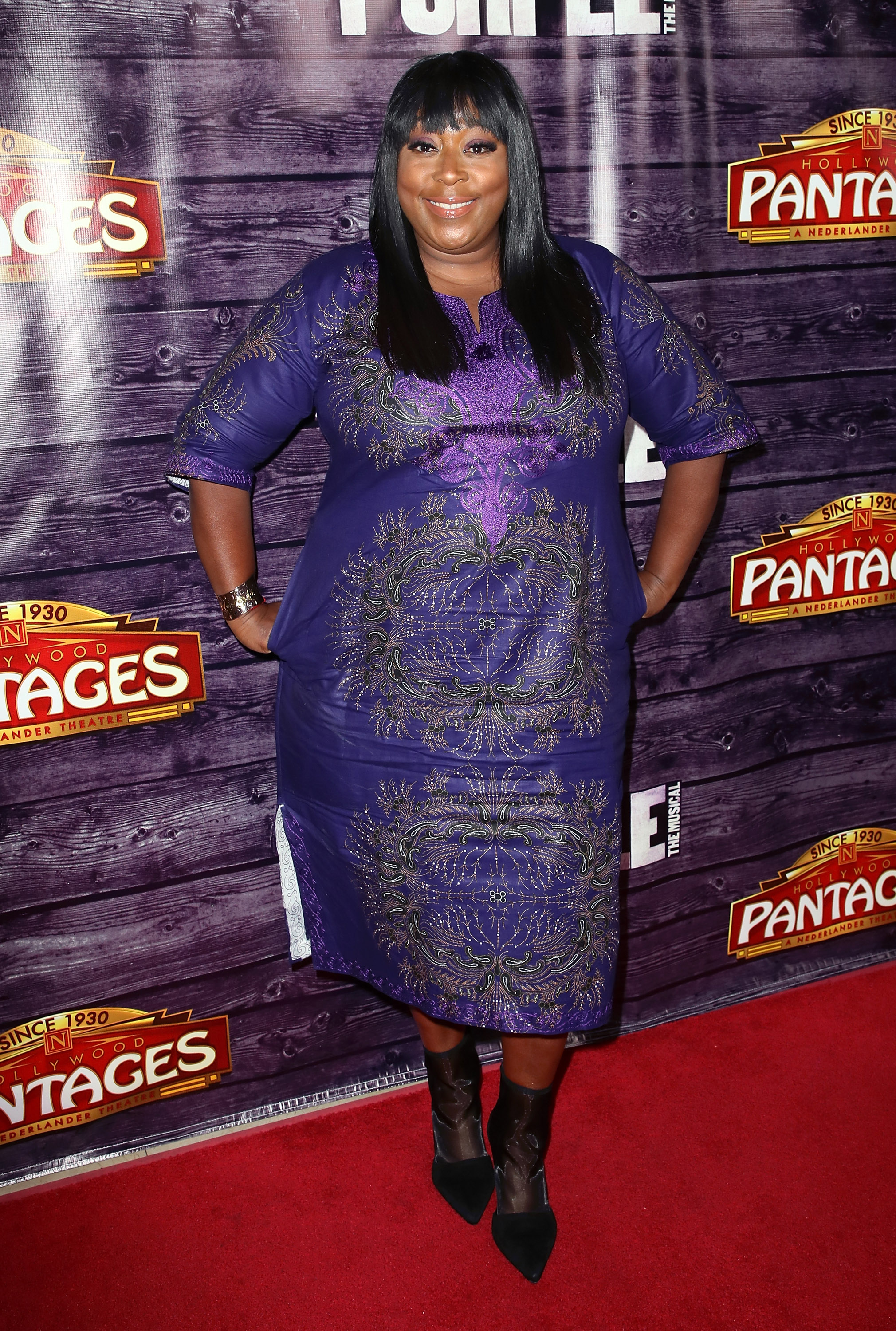 Loni Love attends "The Color Purple" Los Angeles engagement celebration on May 29, wearing a purple embroidered dress, black boots, and a cheerful smile at the Hollywood Pantages Theatre.