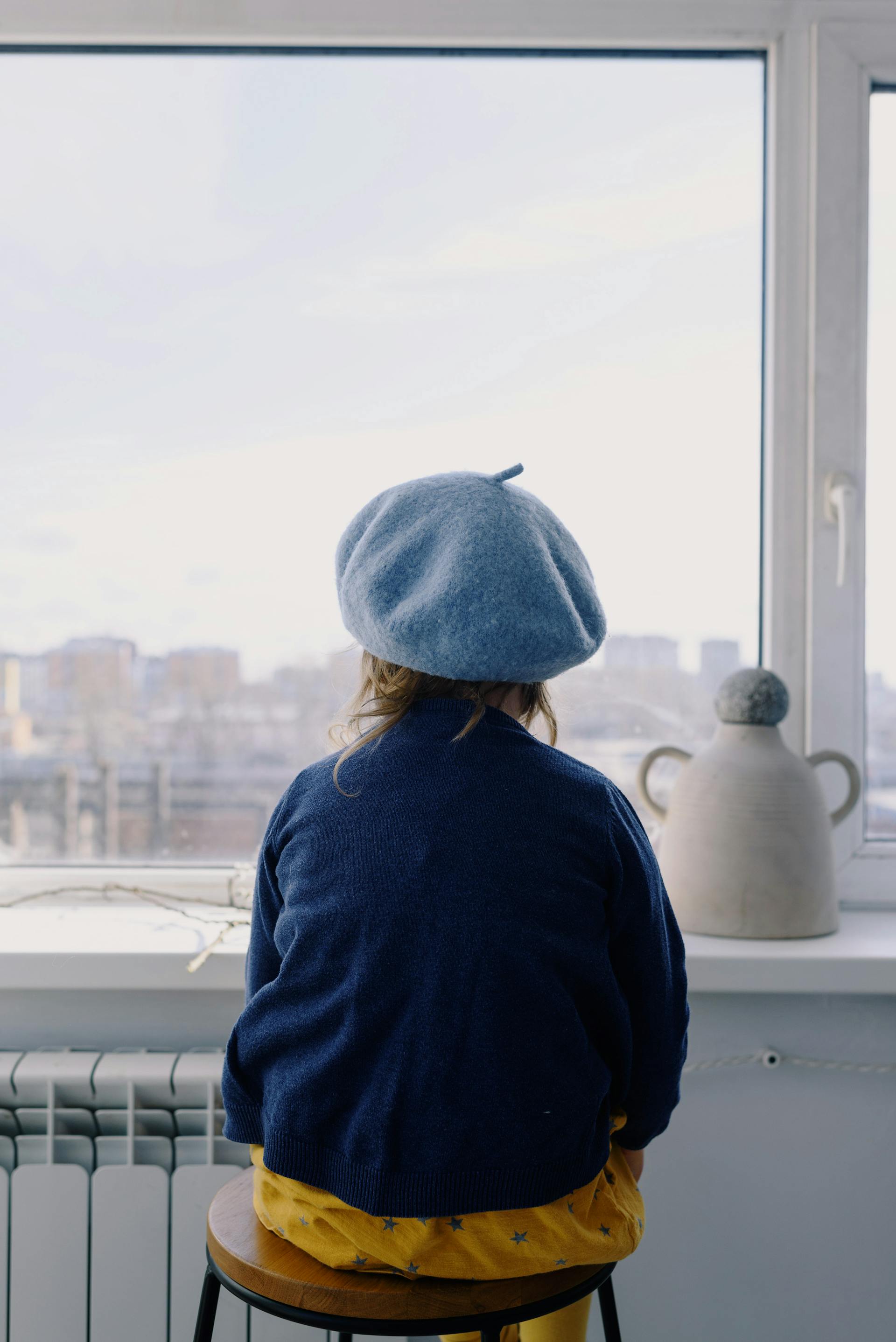 Una niña con una boina mirando afuera desde la ventana | Fuente: Pexels