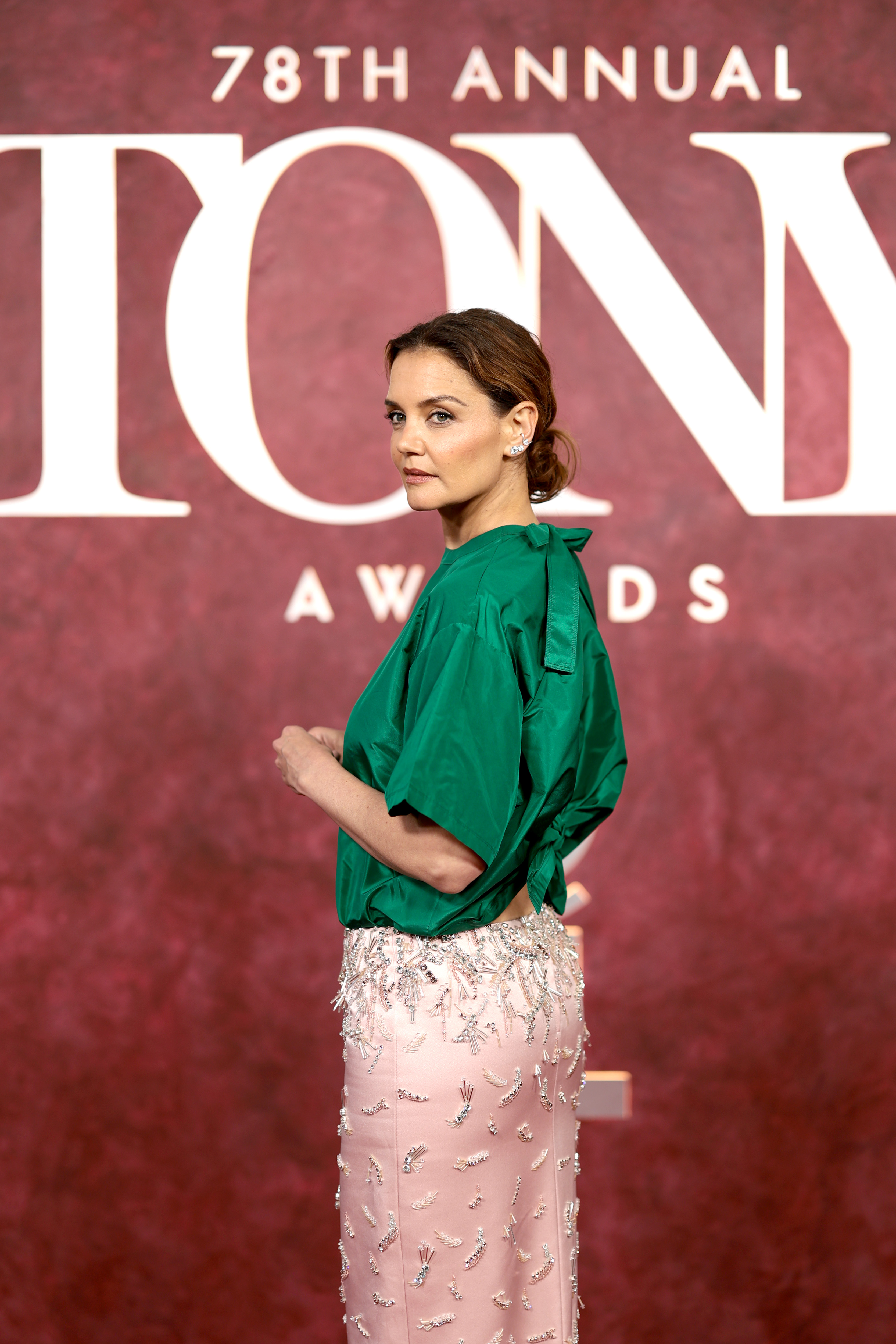 Pausing in profile, Katie Holmes showcases a bold two-tone look — satin green on top, blush pink and silver beadwork below — firmly capturing the attention of fashion watchers and photographers alike.