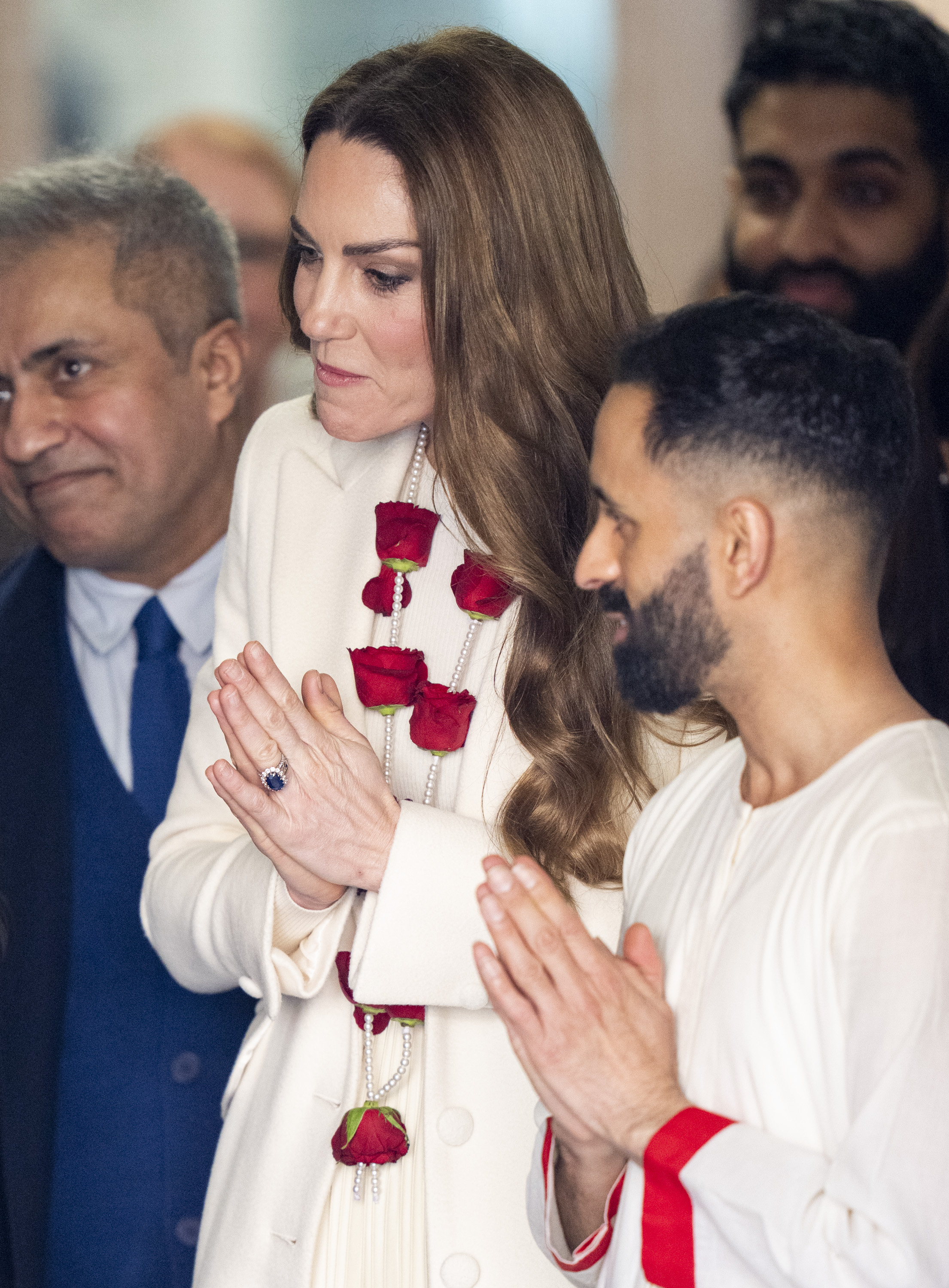 Catherine, Princess of Wales, presses her palms together in a respectful Namaste as she greets those welcoming her inside the Aakash Odedra Company during her visit to Leicester on March 5, 2026. Wearing a striking garland of red roses and pearls draped over her cream outfit, the Princess of Wales mirrors the gesture of those around her in a moment that reflects the cultural traditions woven into the day's celebrations.