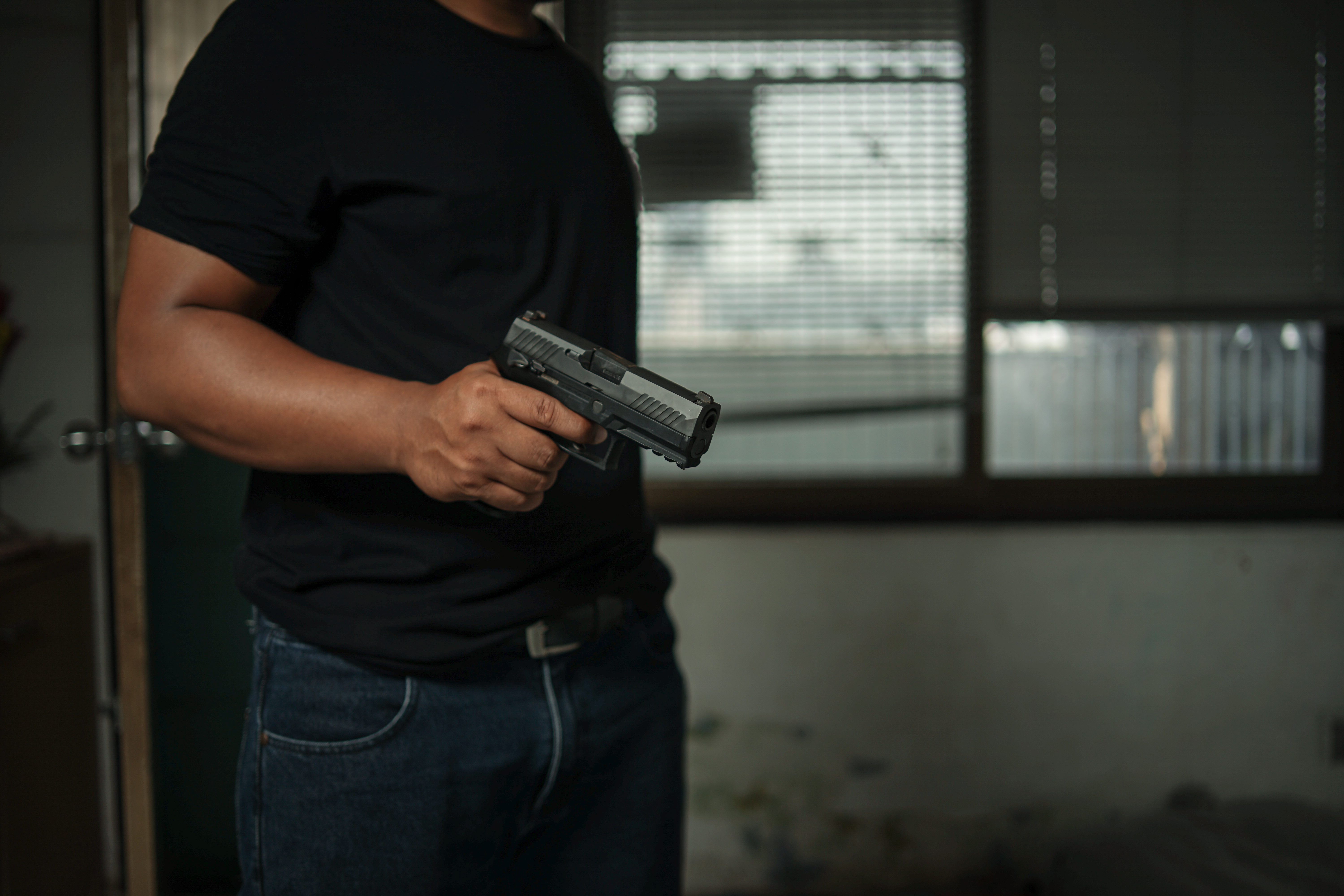 Man holding a pistol, standing in a room in black, pointing and aiming a gun at a target | Source: Shutterstock.com