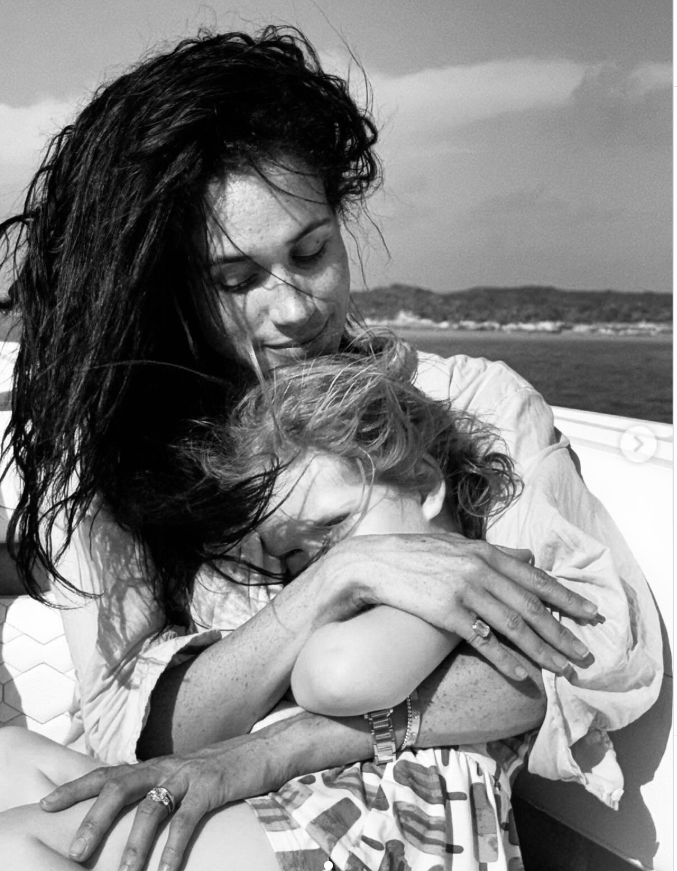 Meghan Markle wraps Princess Lilibet in a protective embrace aboard a boat, creating a serene mother-daughter portrait against a coastal backdrop. | Source: Instagram/meghan