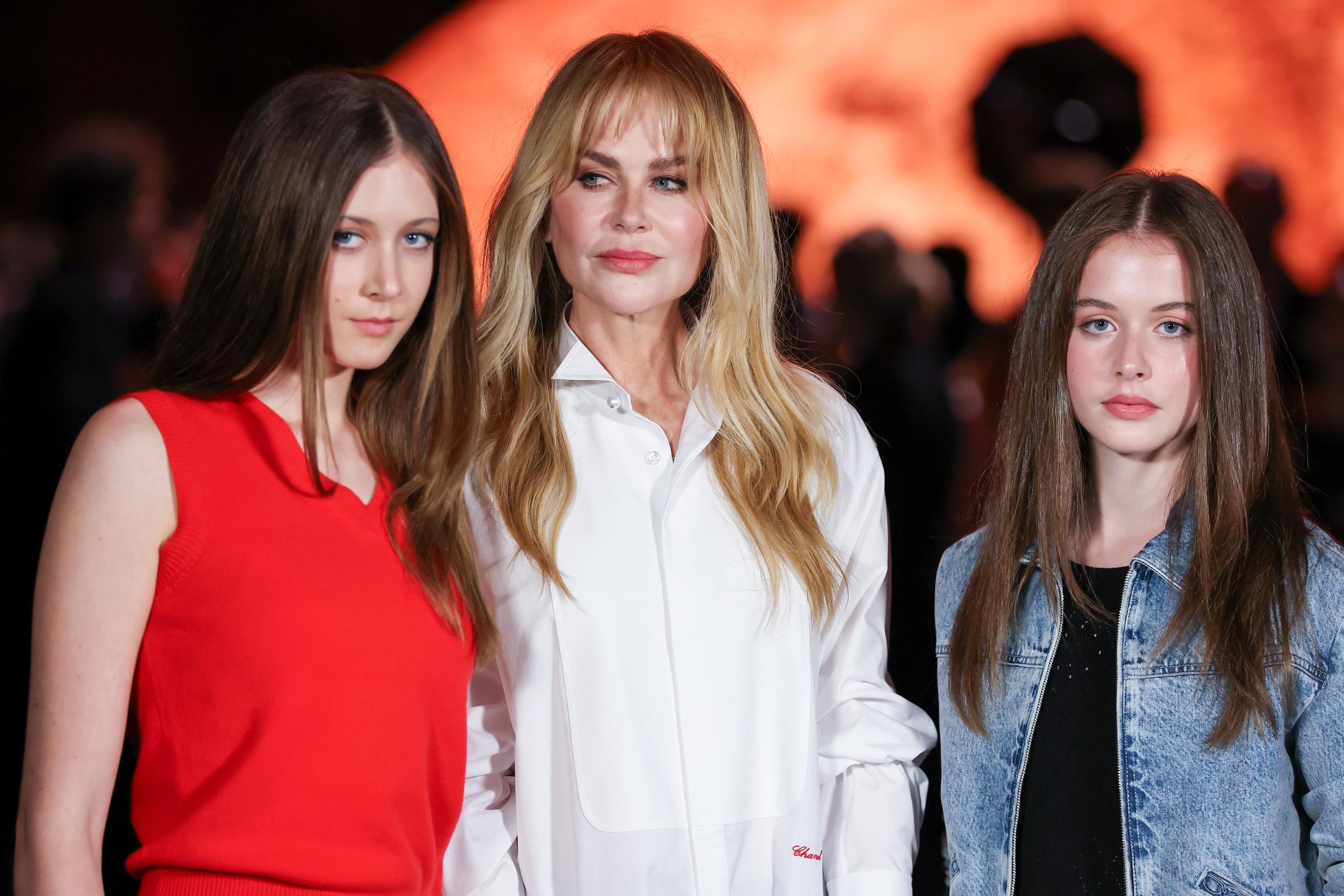 Nicole Kidman appears poised alongside her teenage daughters at the Chanel Womenswear Spring/Summer 2026 show in Paris. The trio faces cameras under the event's warm, glowing light.