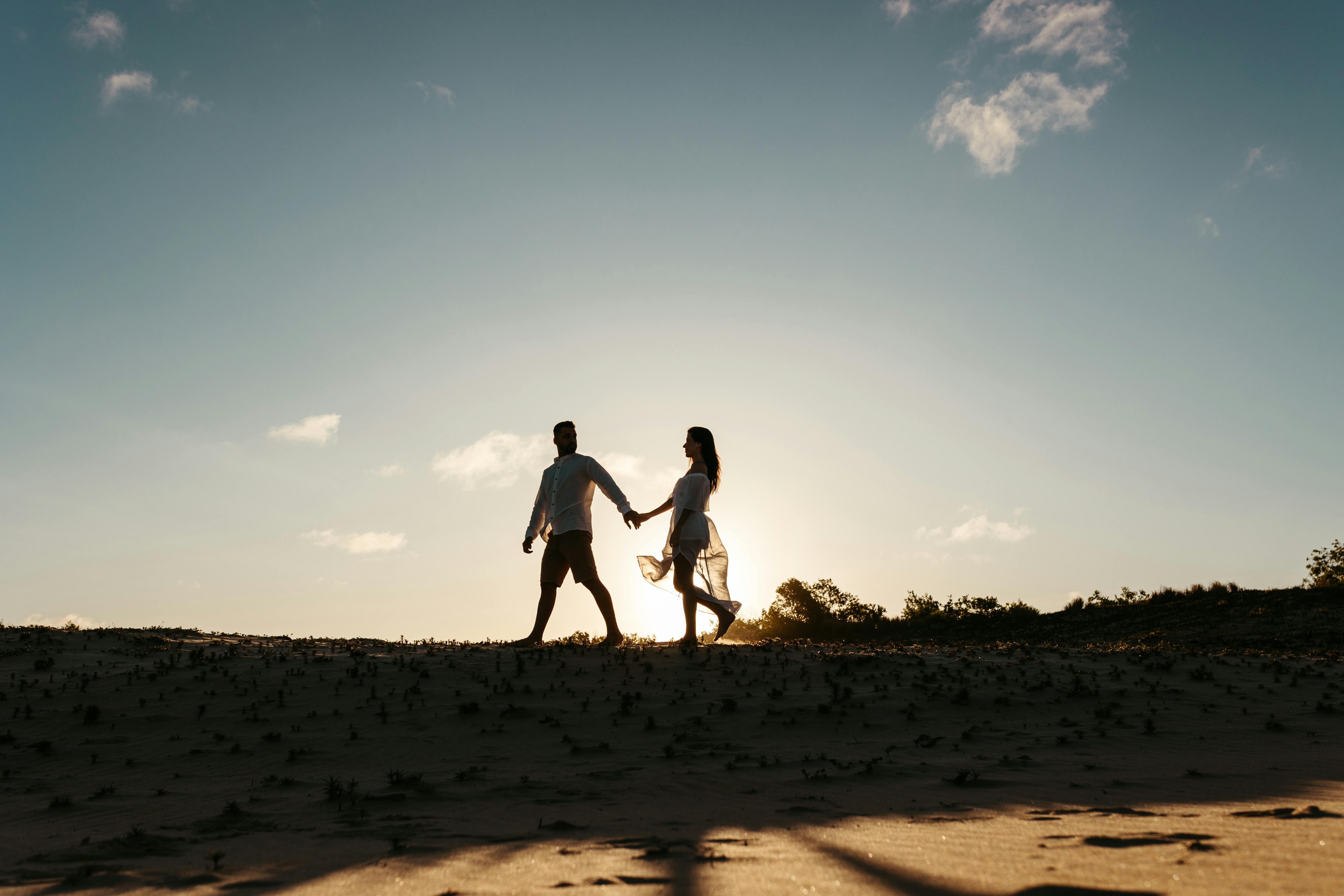 Man and woman walking hand in hand on a sand dune | Source: Pexels